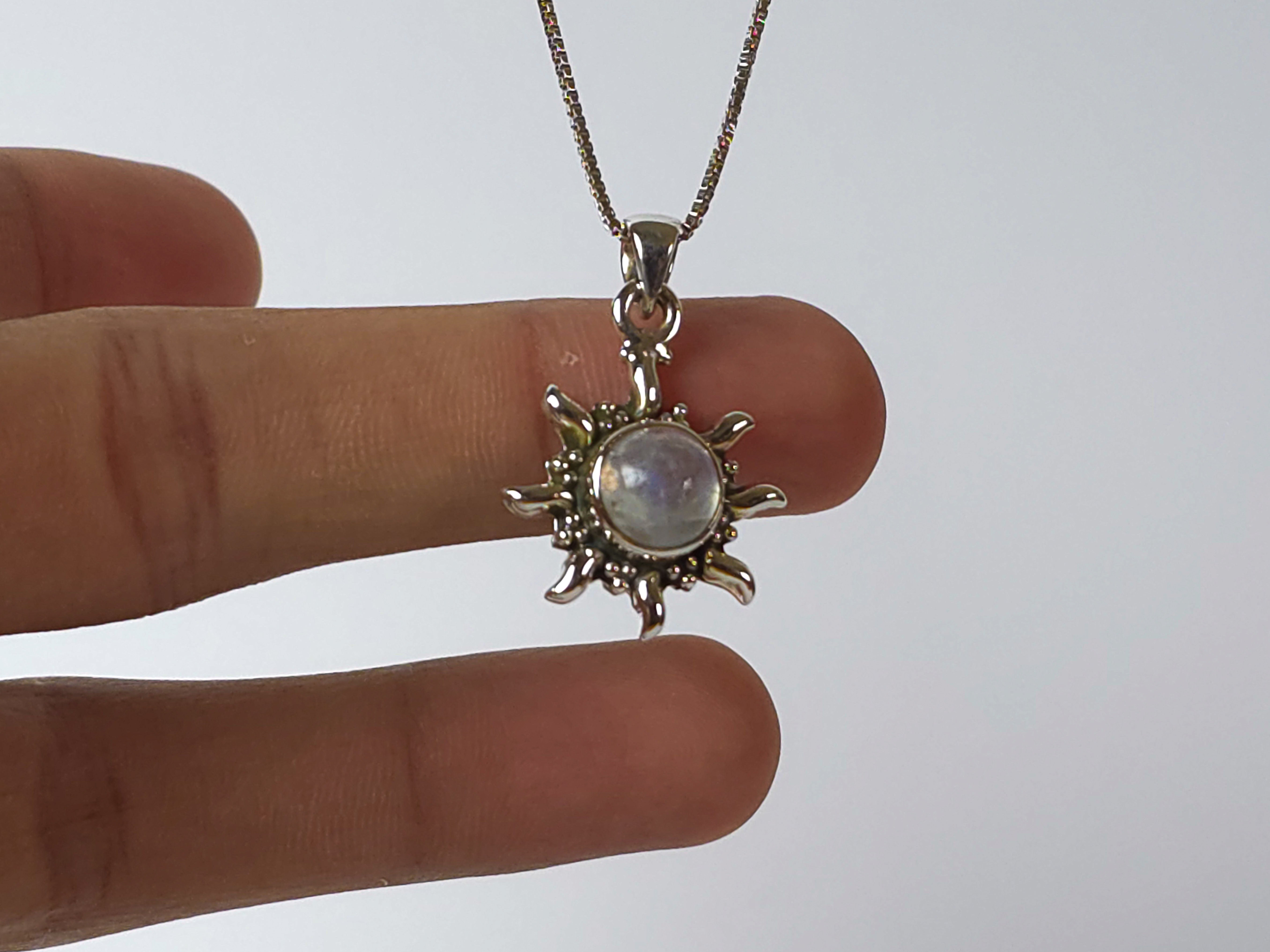 Silver sun-shaped pendant with a central gemstone held between fingers against a white background
