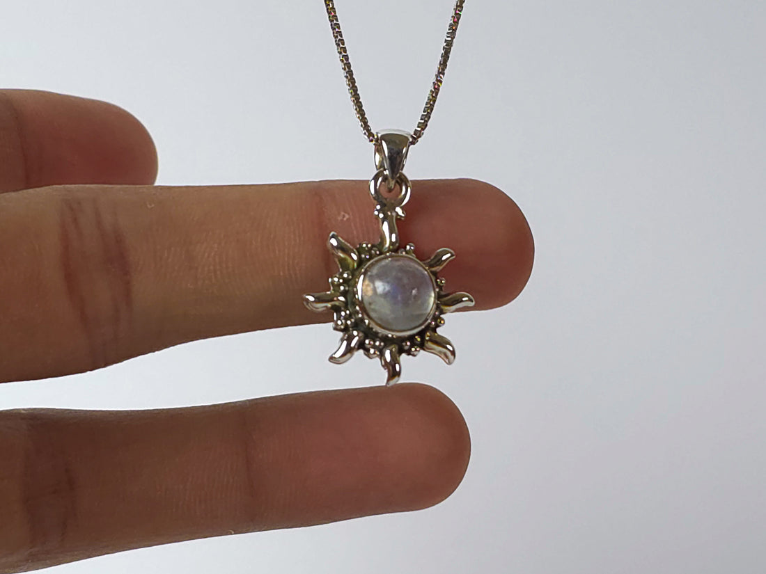 Silver sun-shaped pendant with a central gemstone held between fingers against a white background