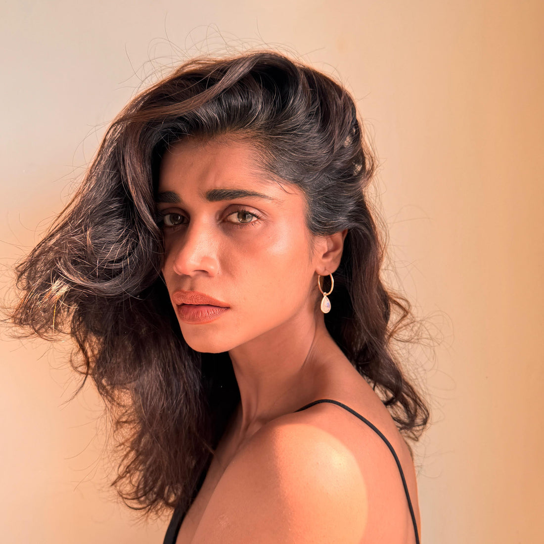 Woman with wavy hair wearing a black top against a beige background