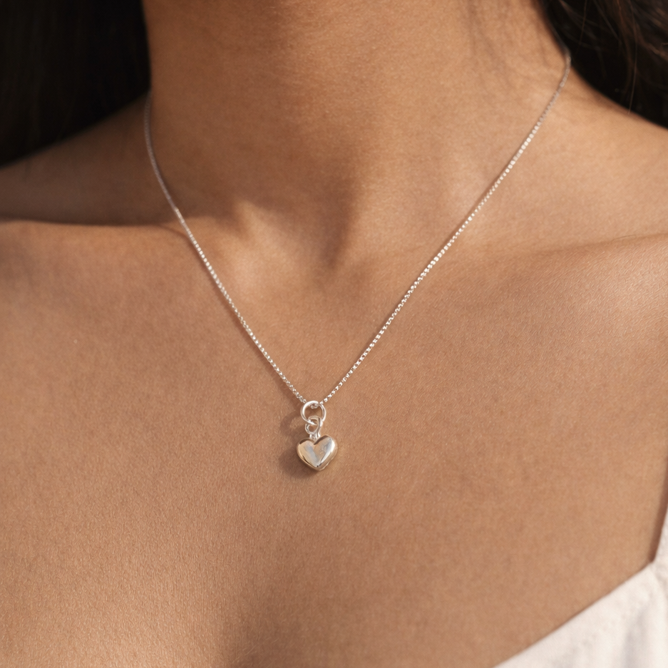 Close-up of a woman wearing a silver necklace with a heart pendant.