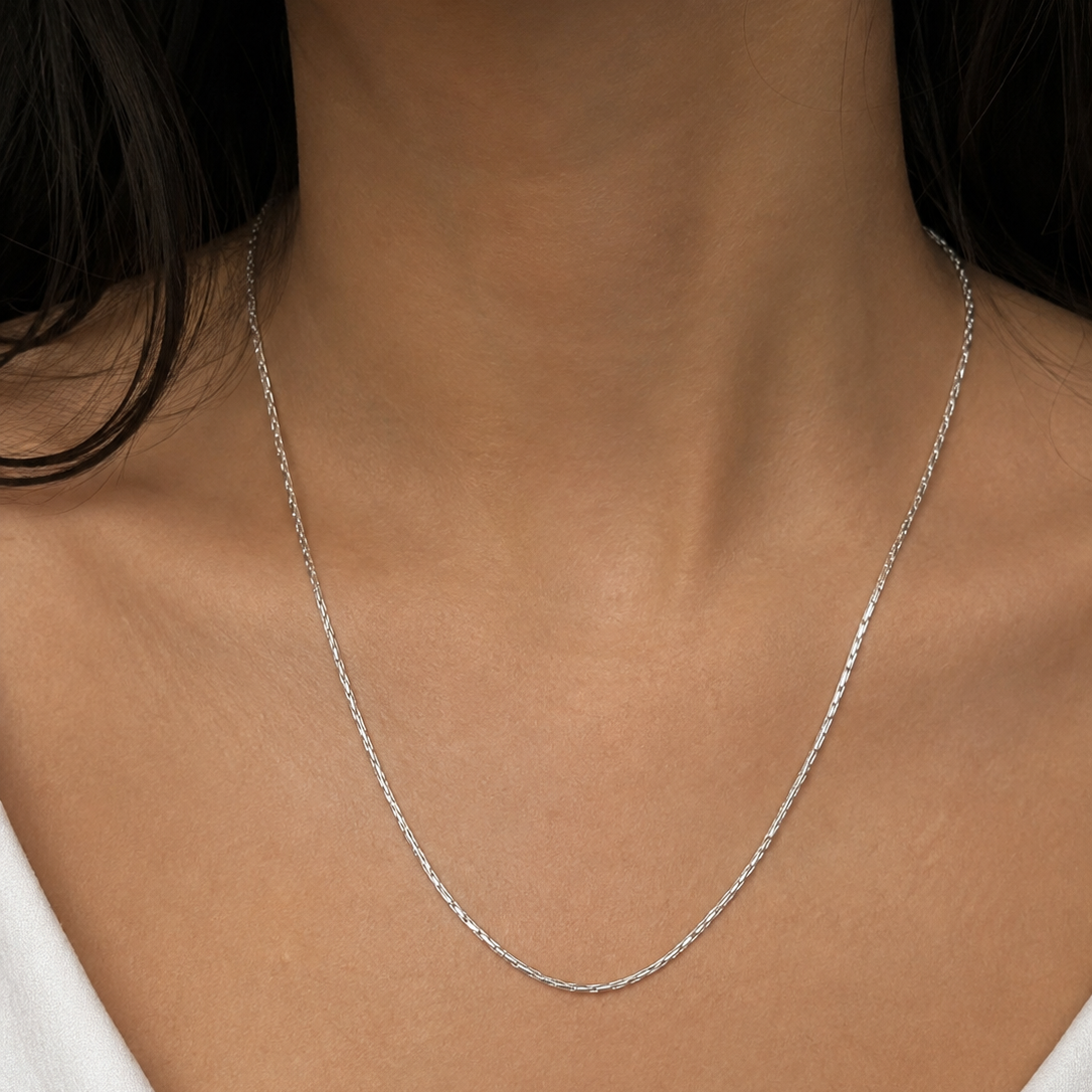 A close-up of a model's neck and upper chest wearing a delicate silver chain necklace.