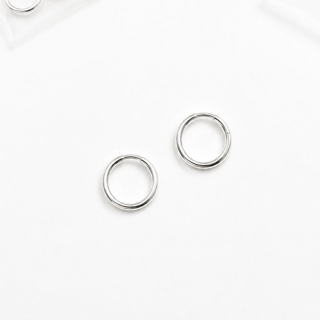 Two silver metal jump rings placed on a clean white surface, with small clear packets containing additional rings partially visible in the top corners.