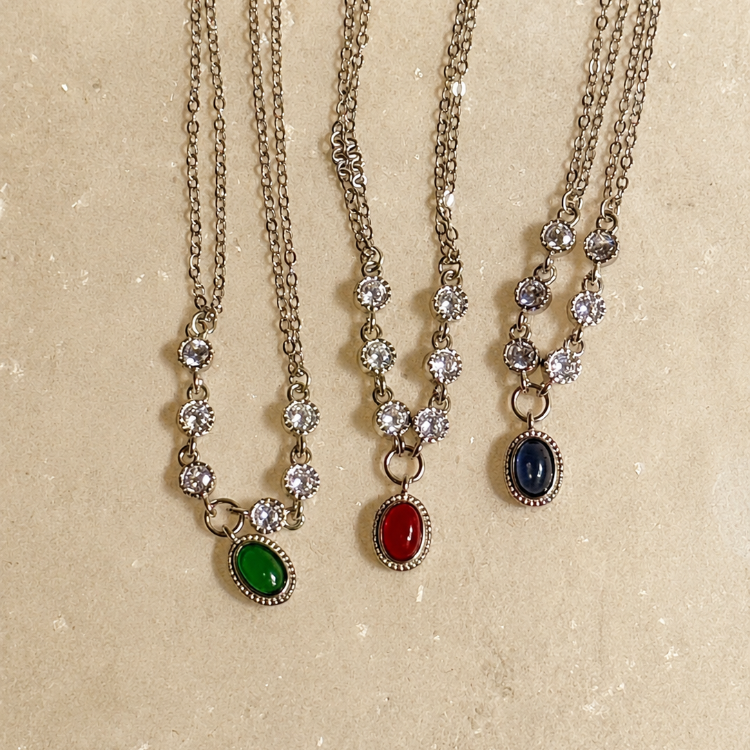 Three necklaces with gemstone pendants on a textured beige background