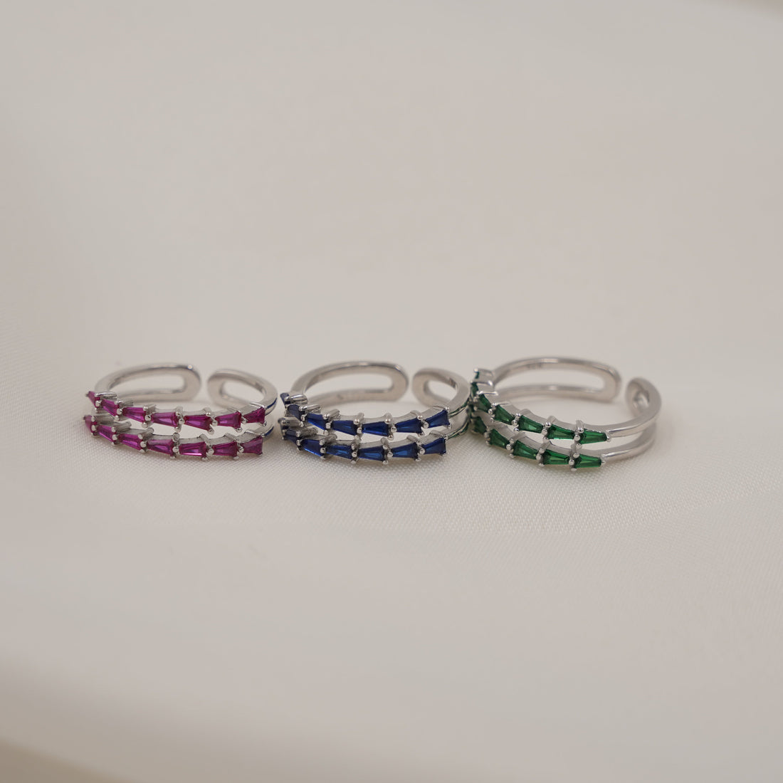 Three silver rings with colorful stones on a white surface