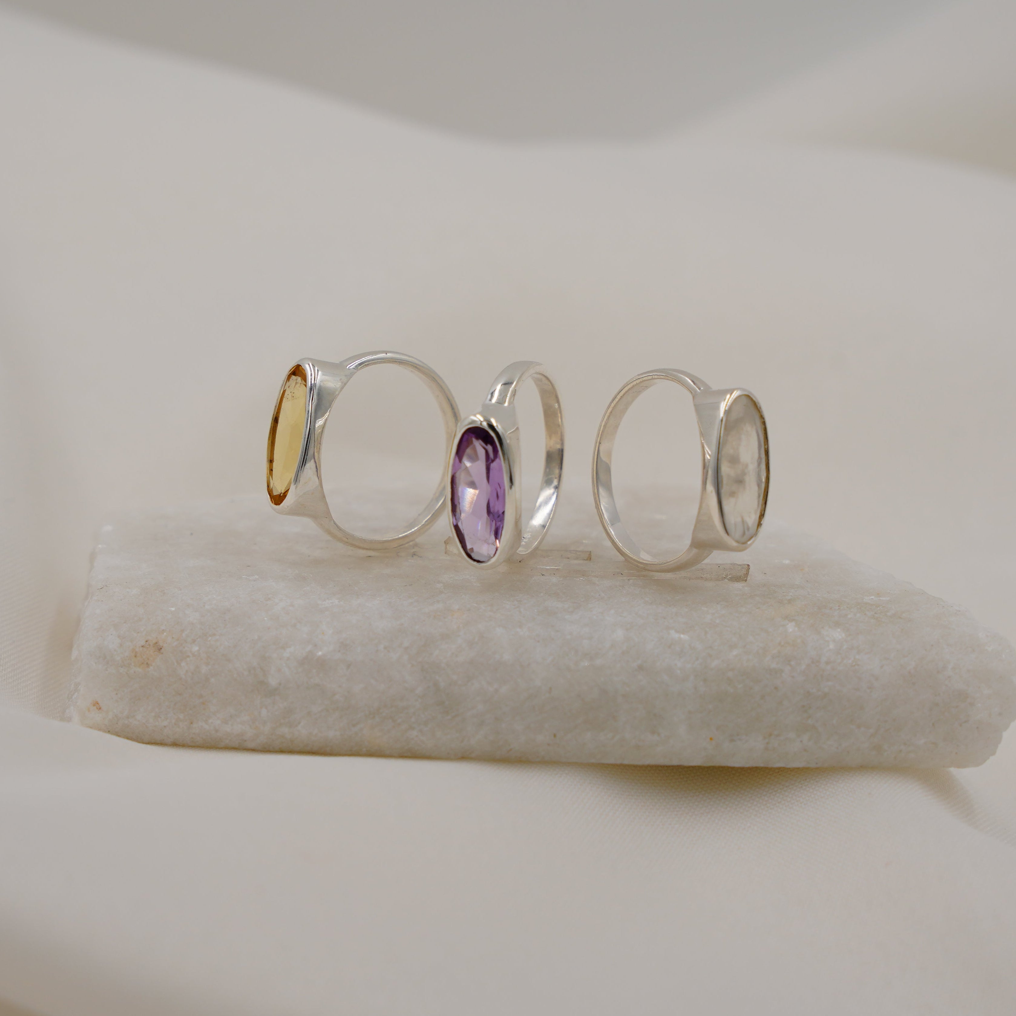 Set of three silver rings with a purple gemstone on a white stone surface