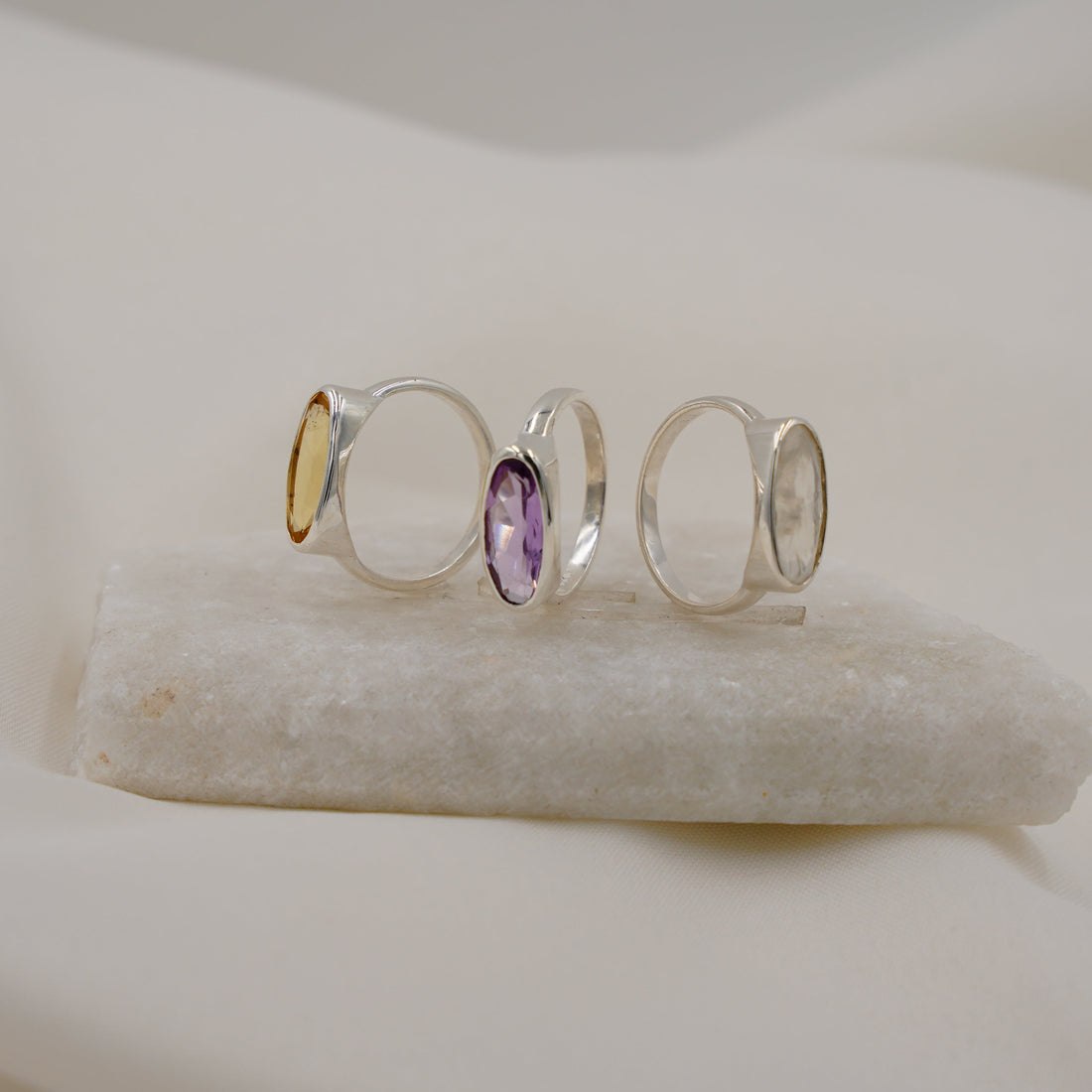 Set of three silver rings with a purple gemstone on a white stone surface