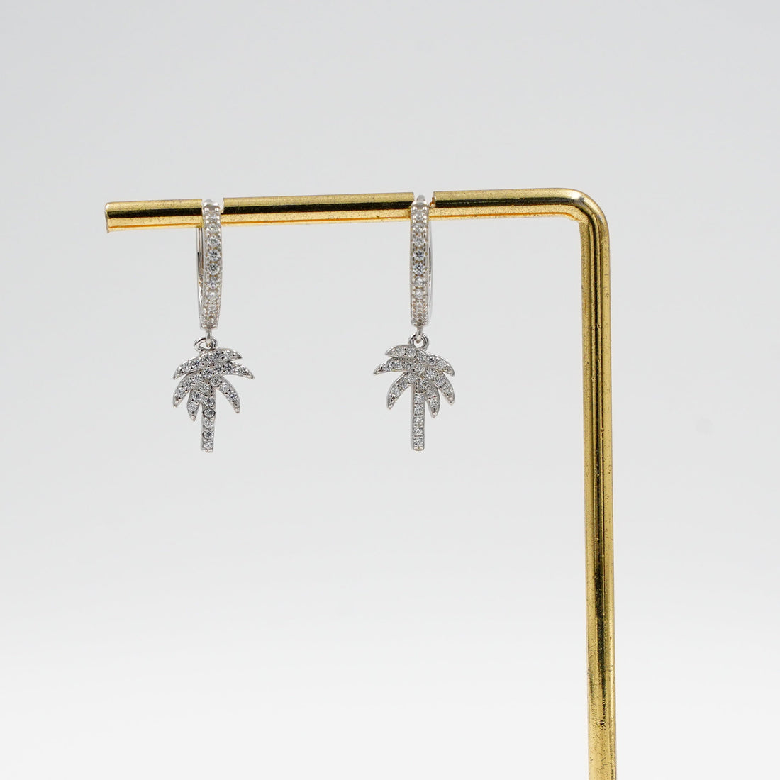 Gold earring stand with wooden base holding silver earrings on a white background