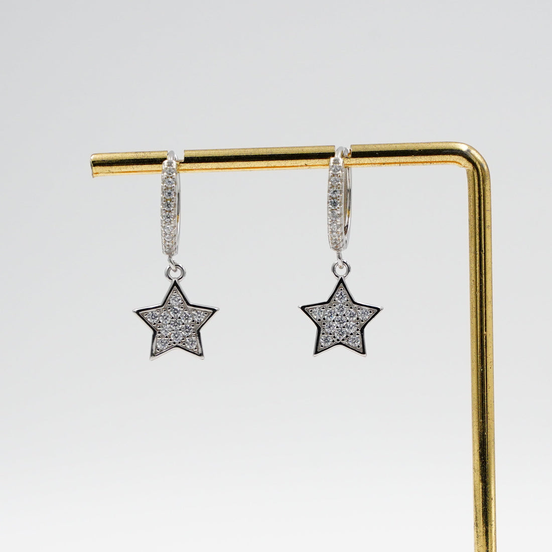Star-shaped earrings on a gold stand with a wooden base against a white background