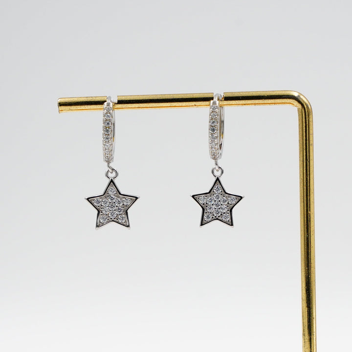 Star-shaped earrings on a gold stand with a wooden base against a white background