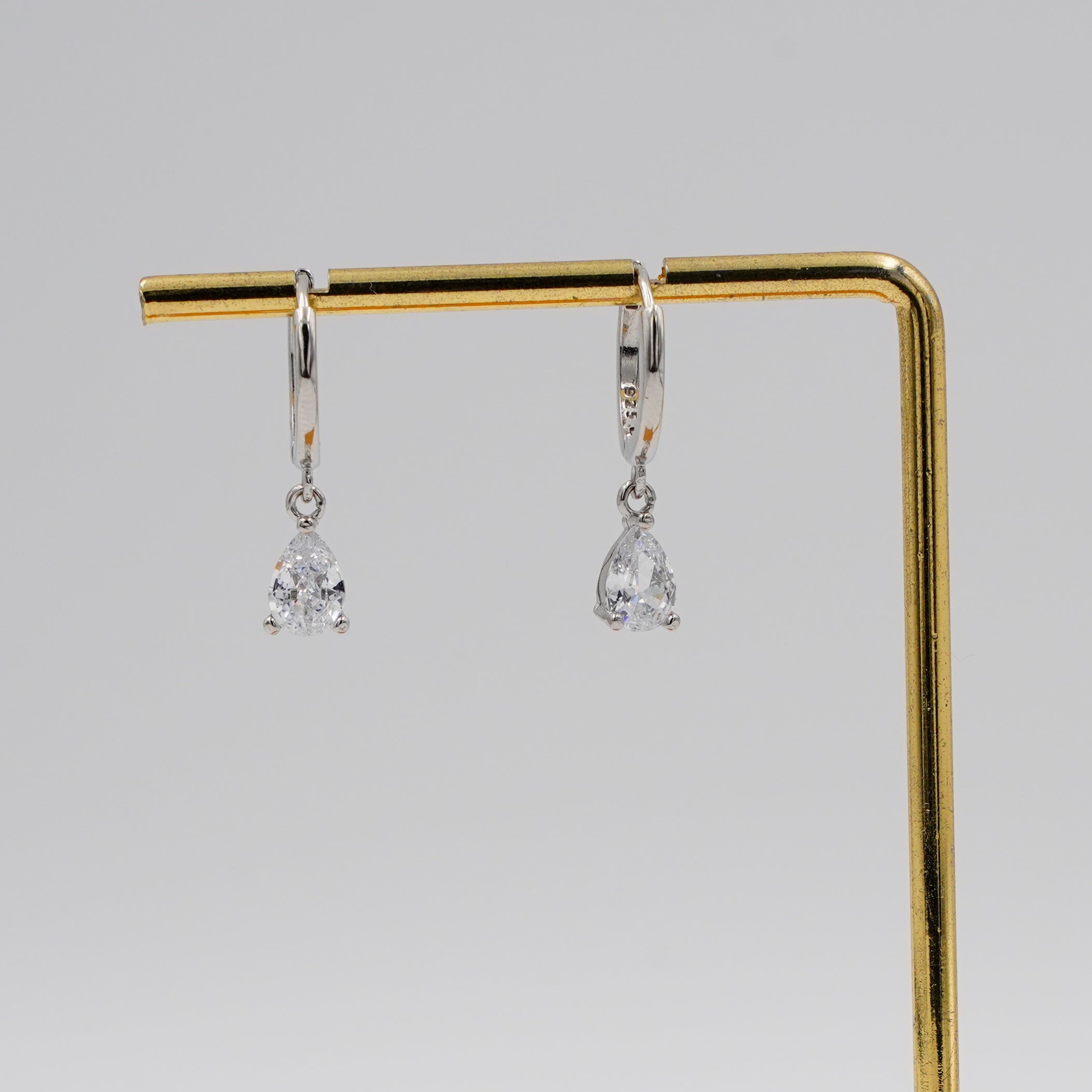 Pair of silver earrings on a gold and wooden stand against a gray background