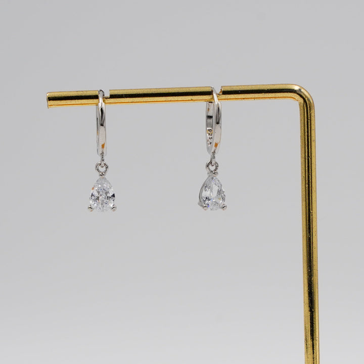 Pair of silver earrings on a gold and wooden stand against a gray background