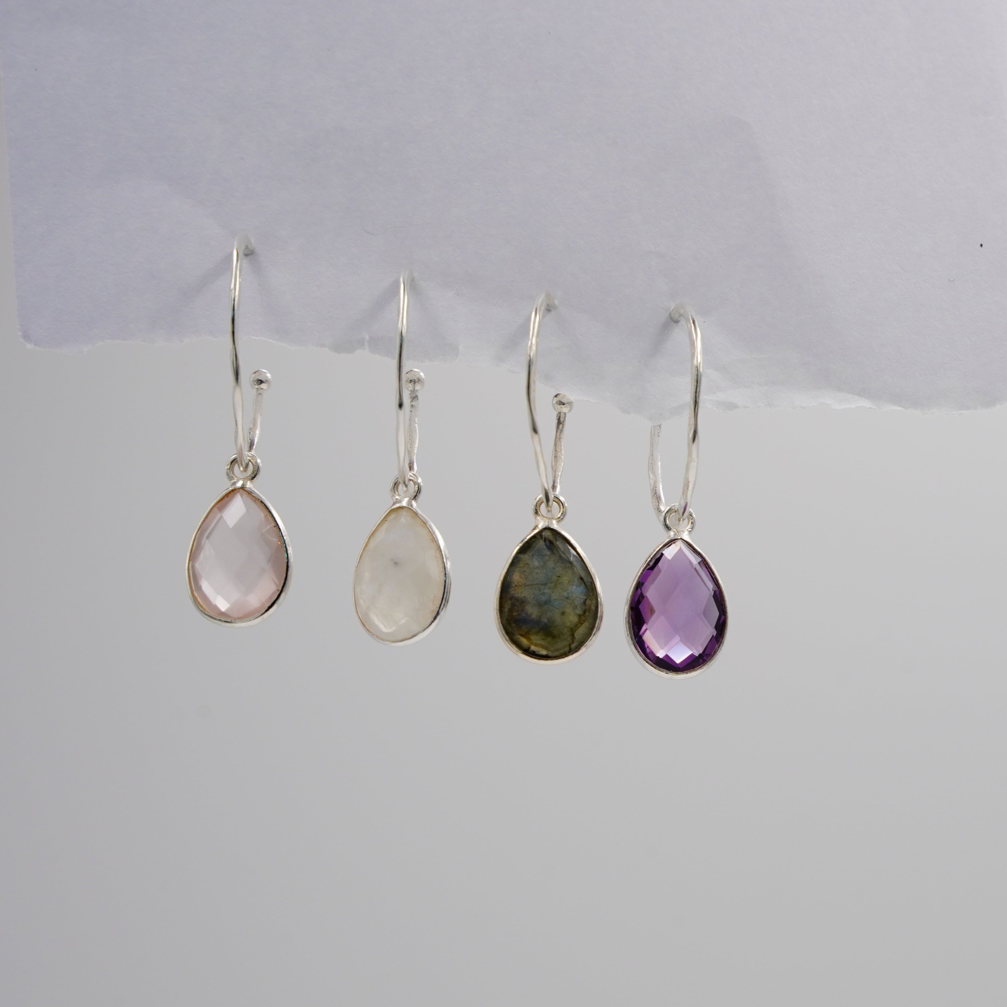 Four pairs of teardrop-shaped earrings with different colored stones on a white background