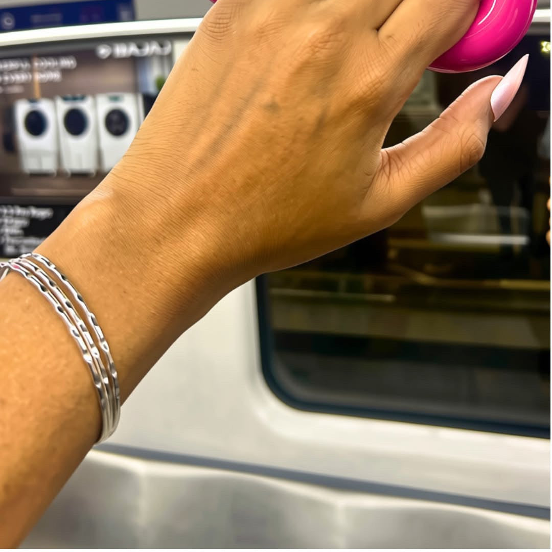 A close-up of a person's hand holding onto a bright pink subway handrail inside a train, wearing a silver ring with a blue stone and a silver bracelet.