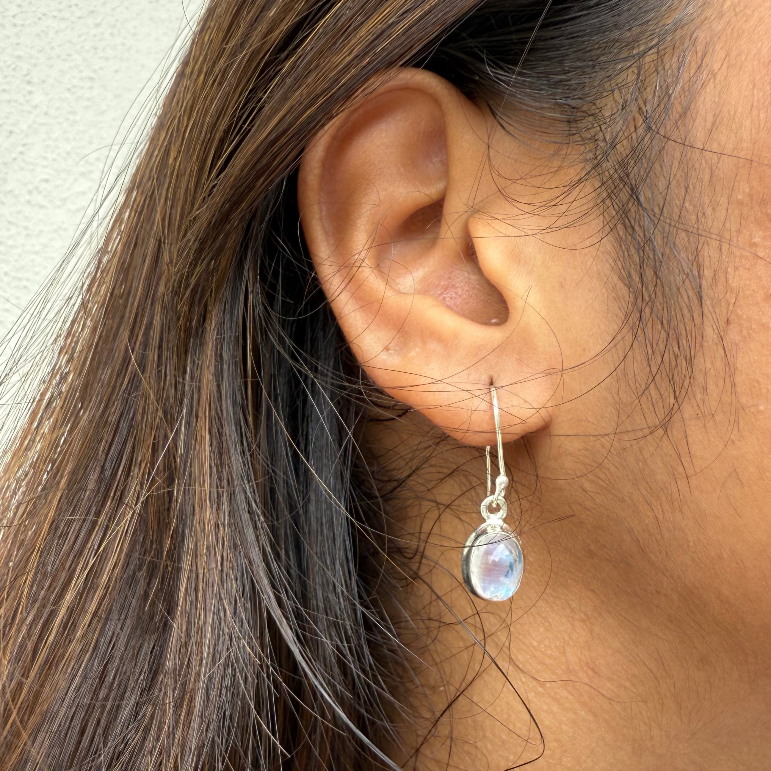Close-up of an ear wearing a silver earring with a clear gemstone.