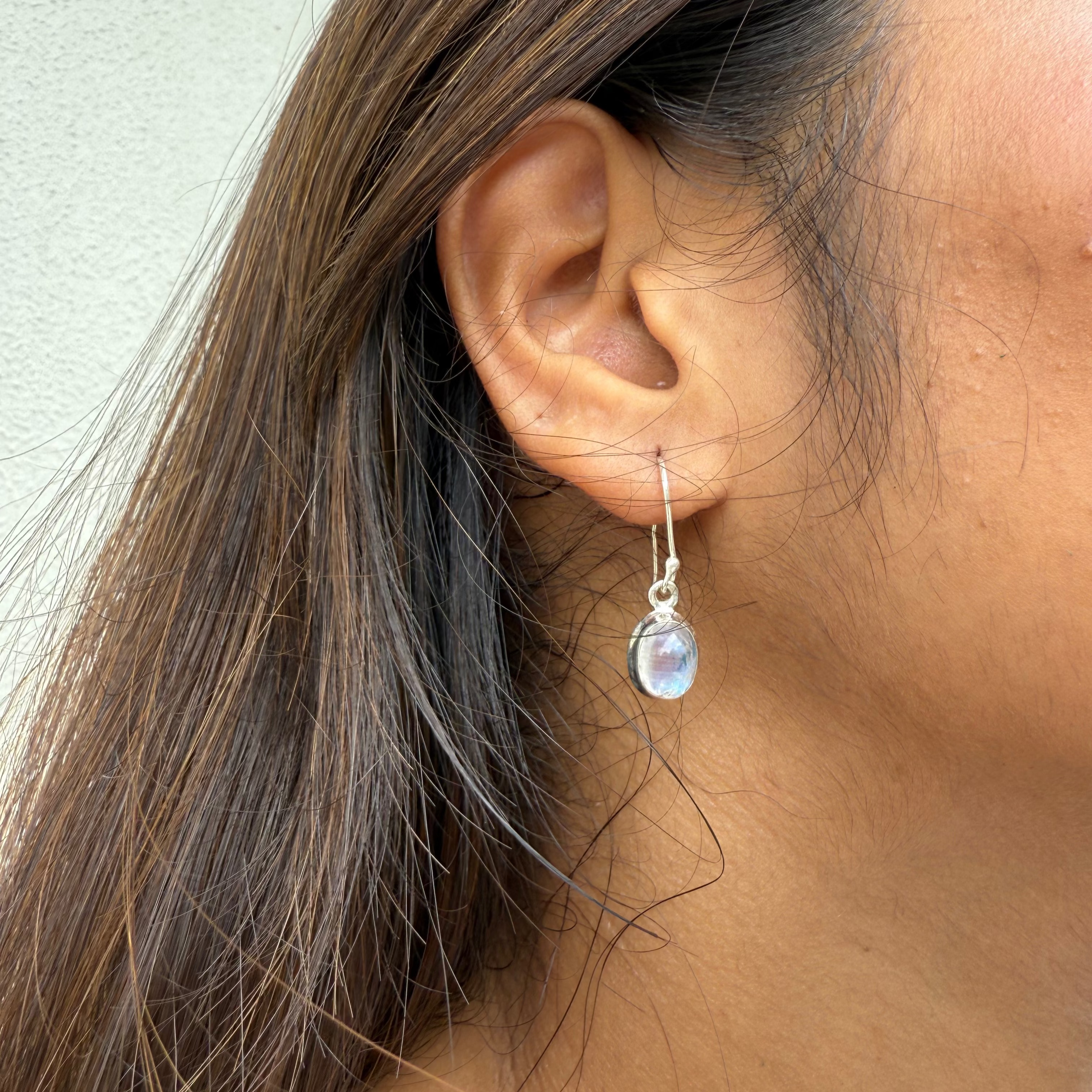 Close-up of an ear wearing a silver earring with a clear gemstone.