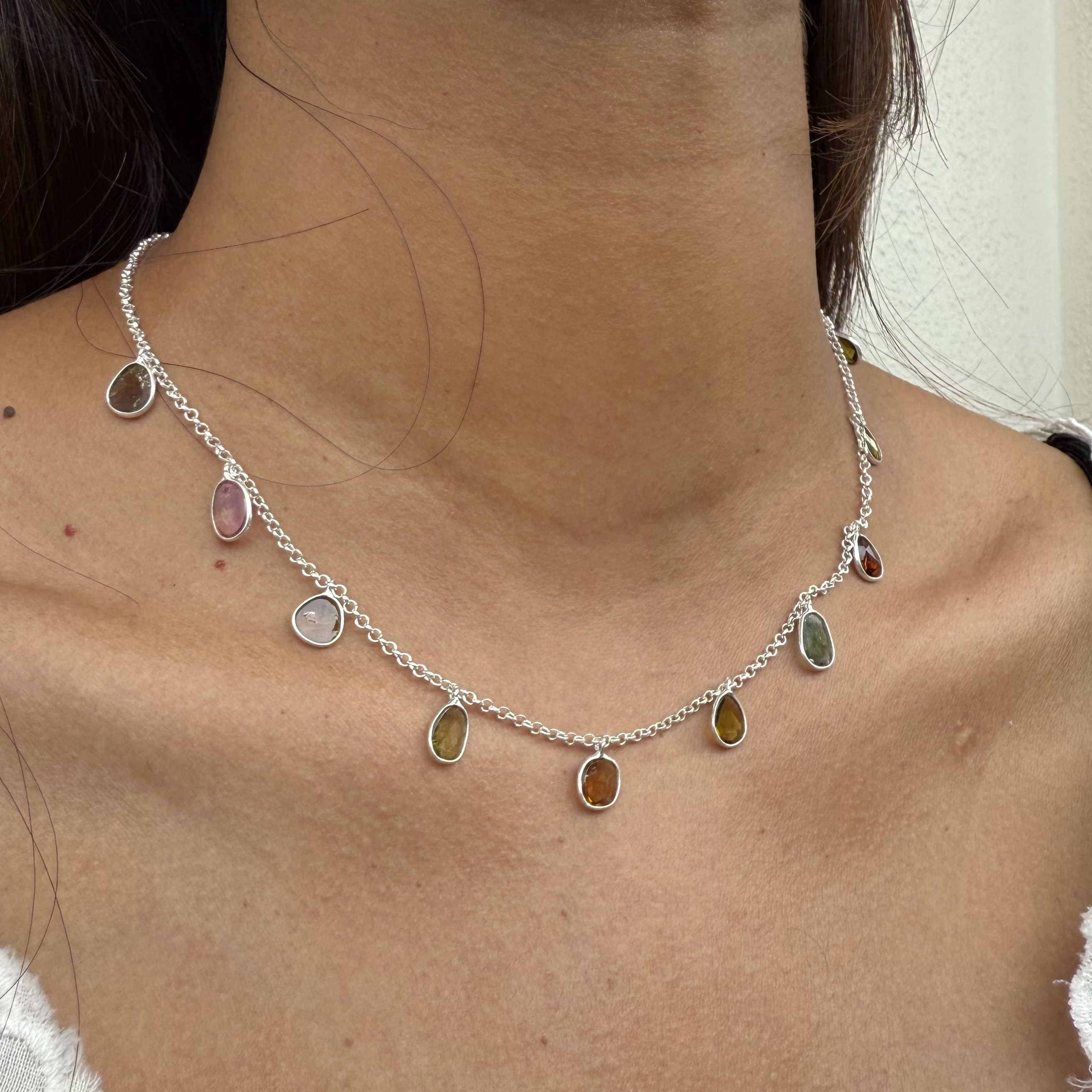 Necklace with multicolored stones worn by a person in a white lace garment.