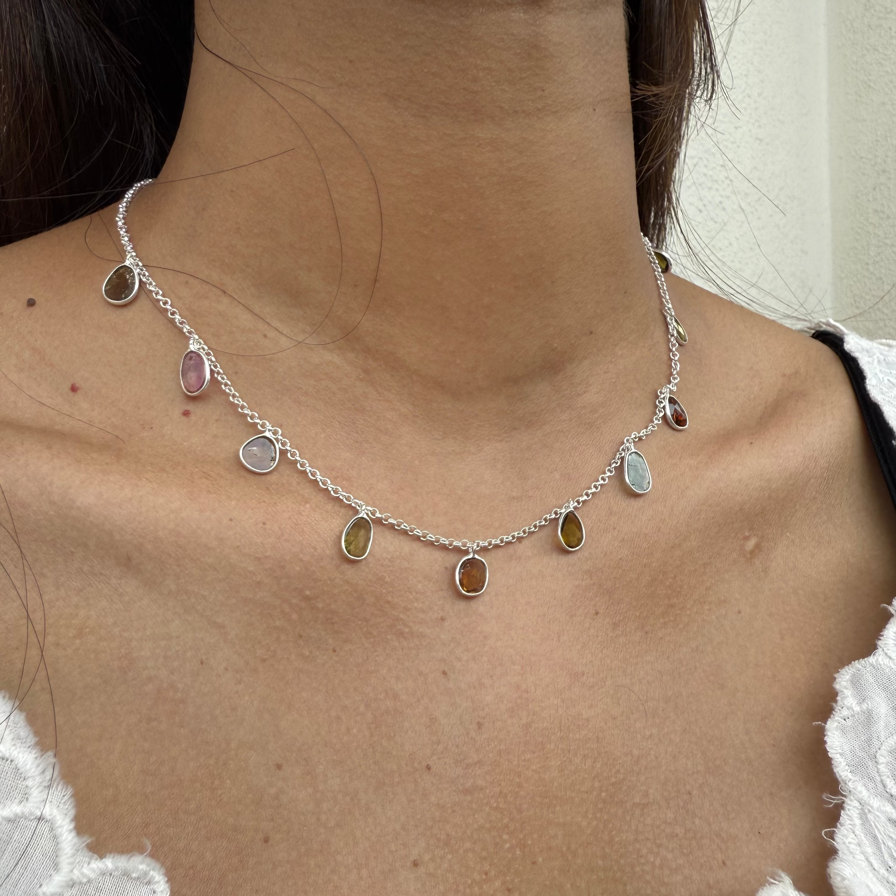 Necklace with multicolored stones worn by a person against a neutral background