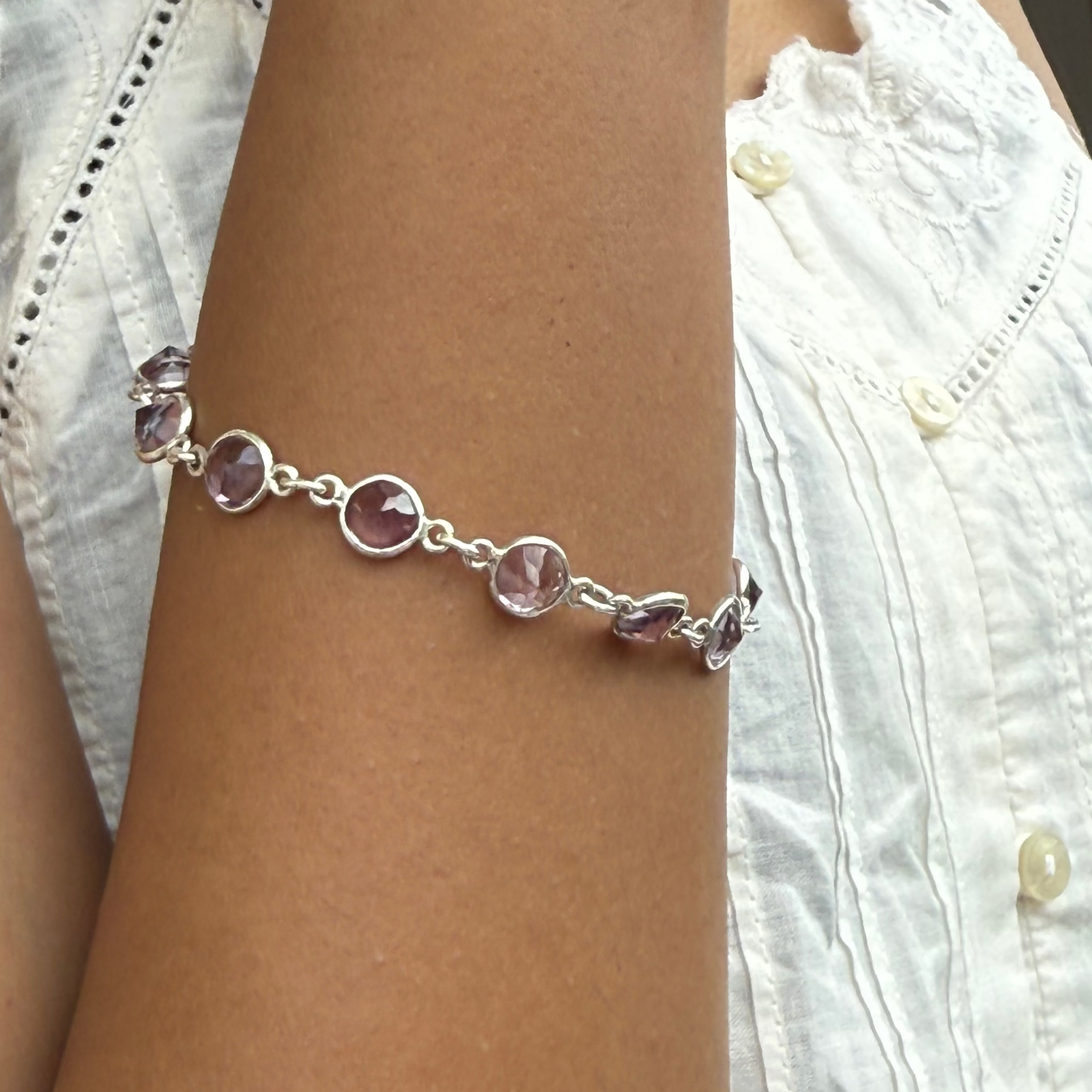 Bracelet with pink beads on a wrist, wearing a white lace top.