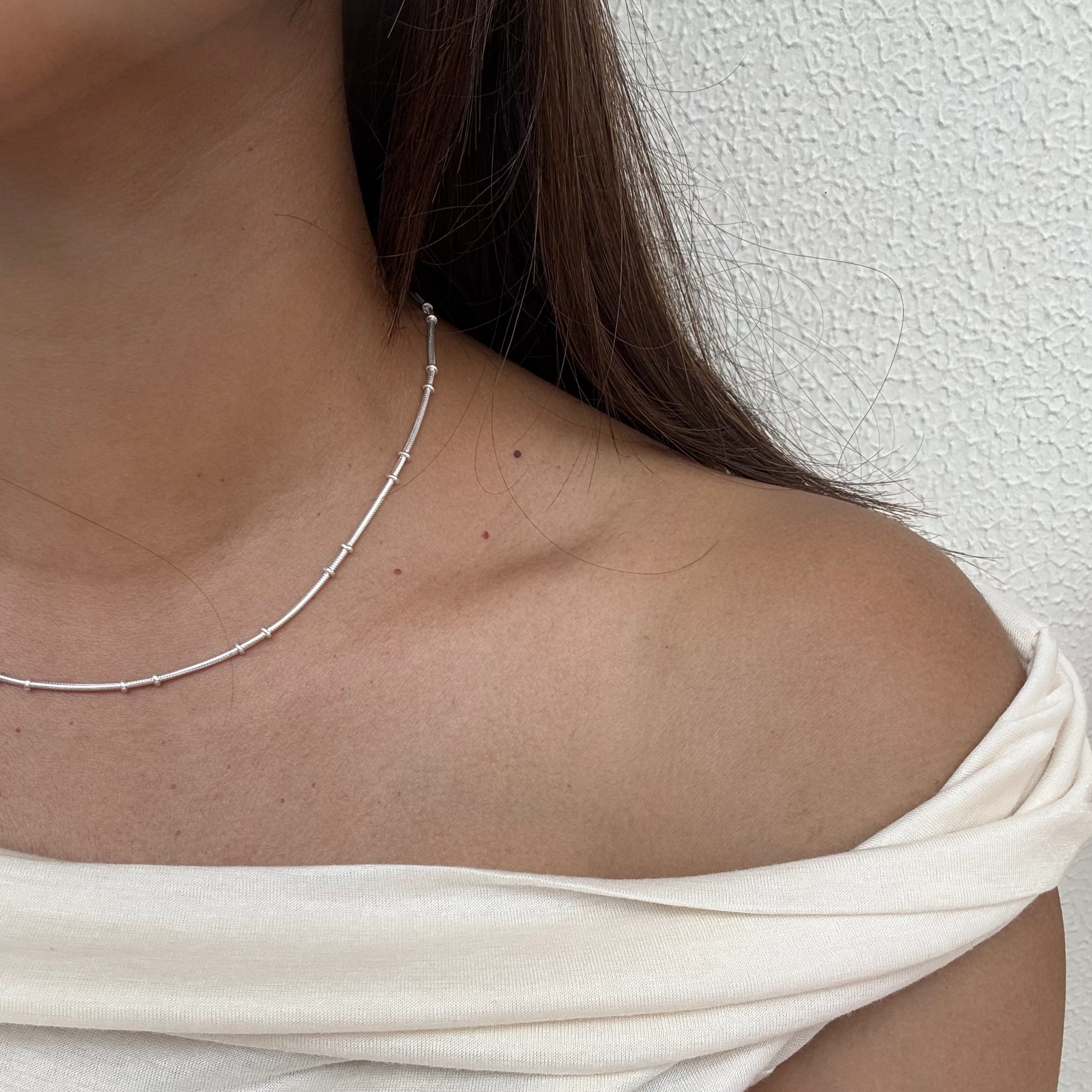 Close-up of a person wearing a delicate silver necklace against a neutral background