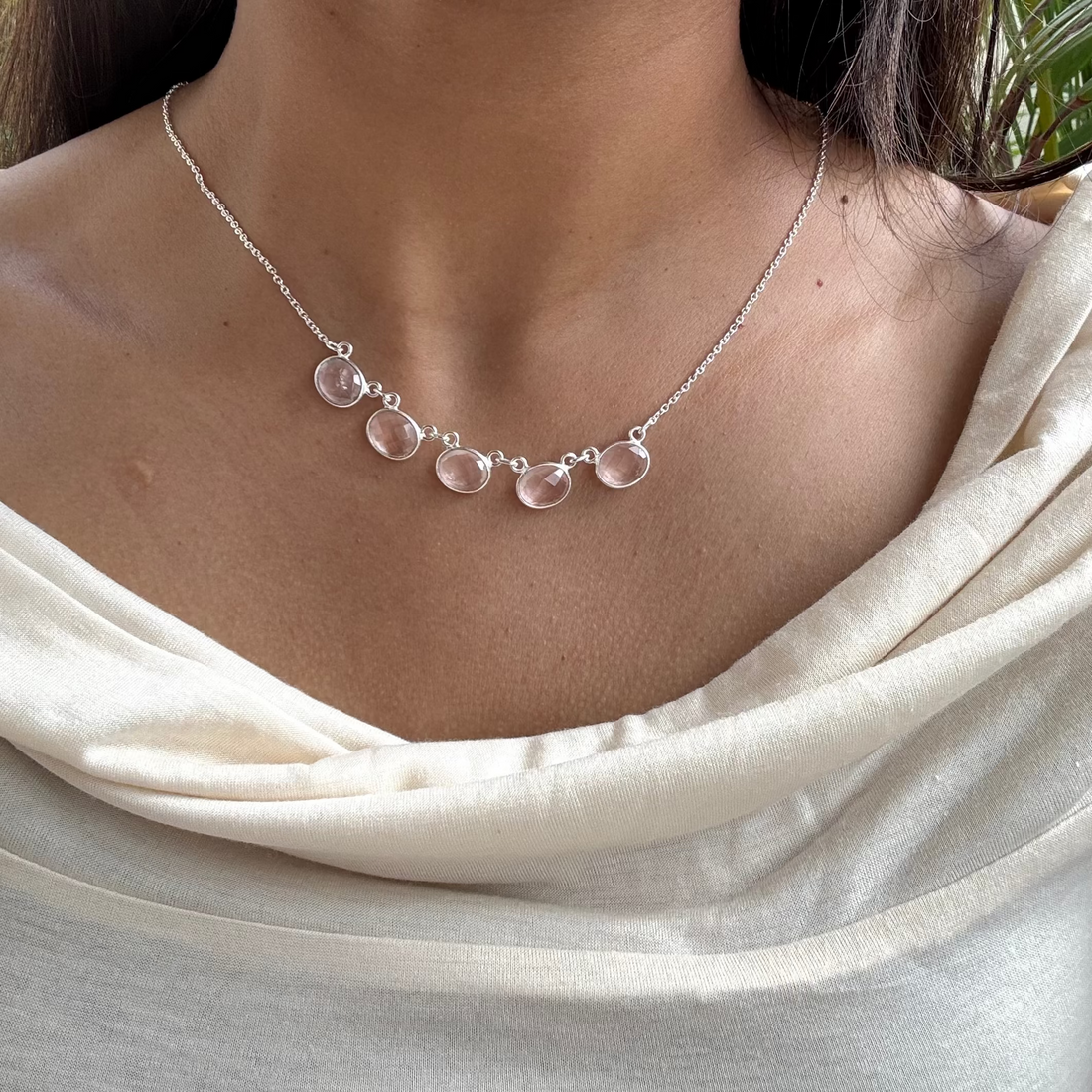 Necklace with clear gemstones worn by a person in a light-colored top.