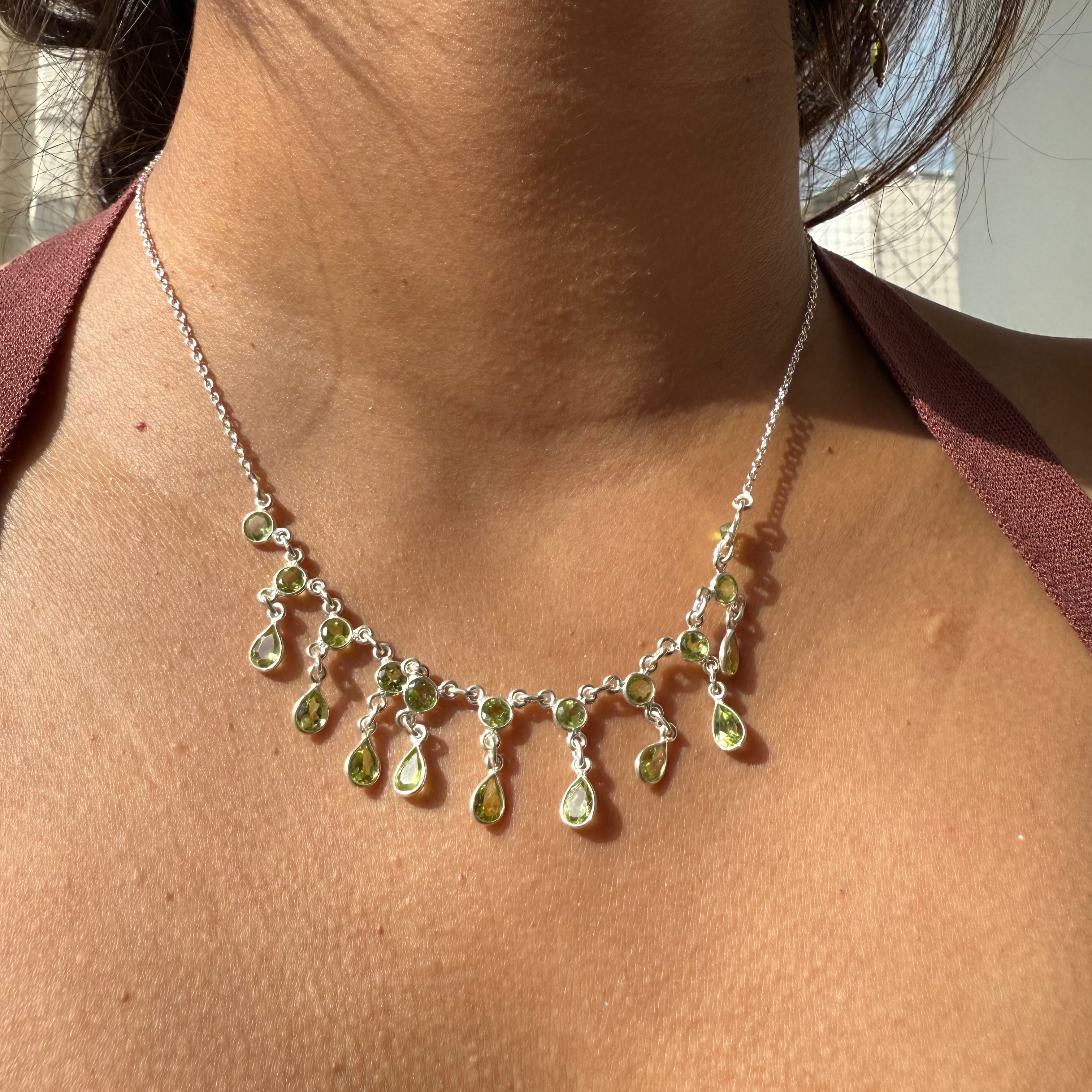 Necklace with green teardrop pendants on a person wearing a red top.