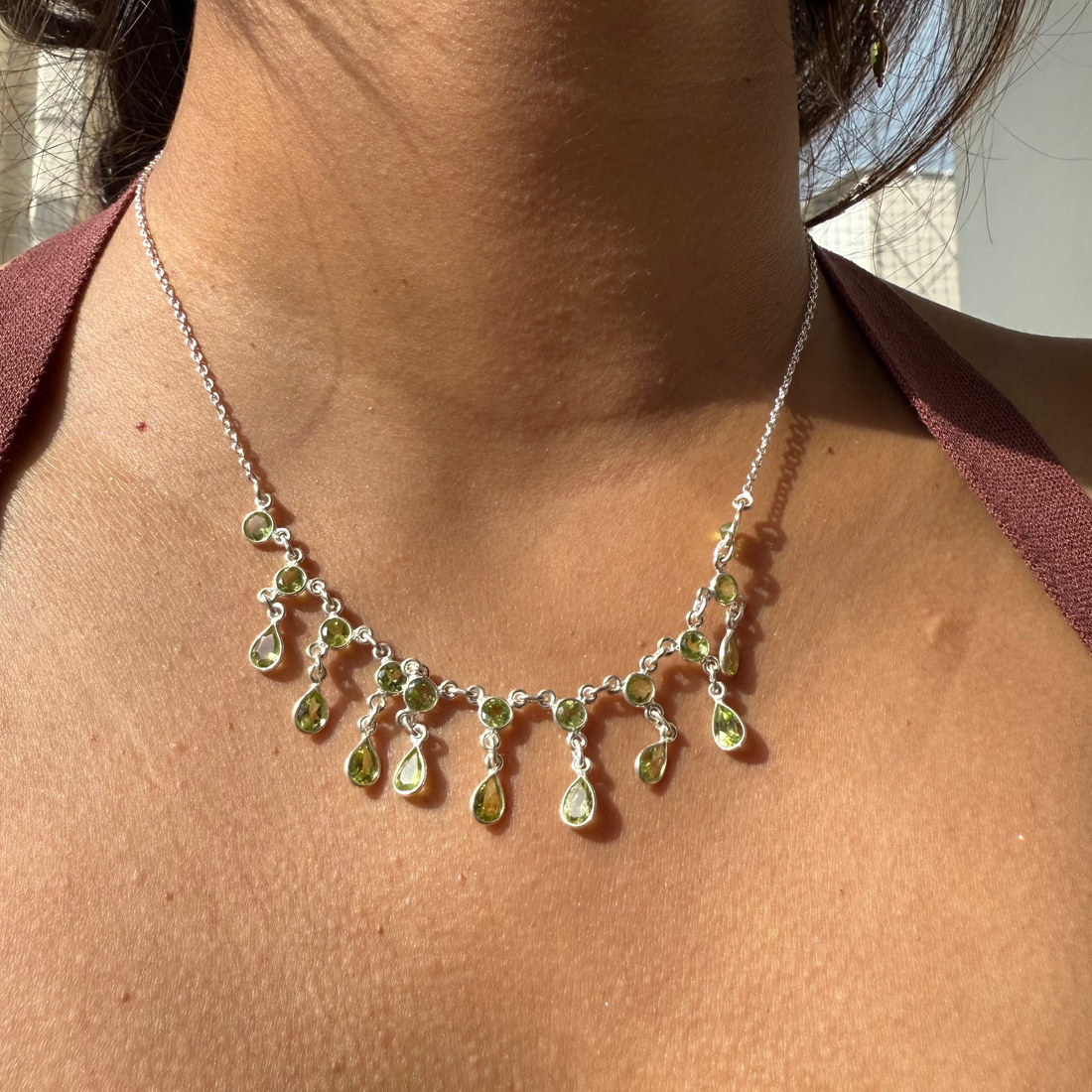 Necklace with green teardrop pendants on a person wearing a red top.