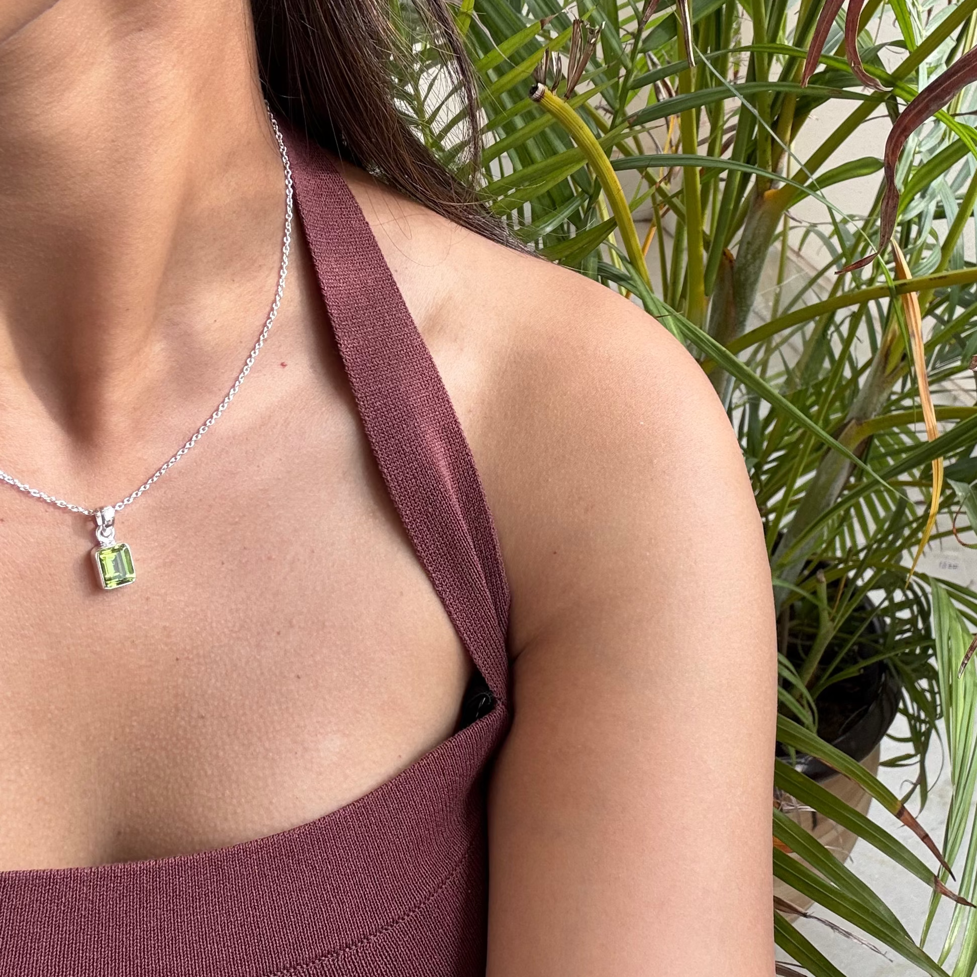 Woman wearing a necklace with a green gemstone in front of a plant