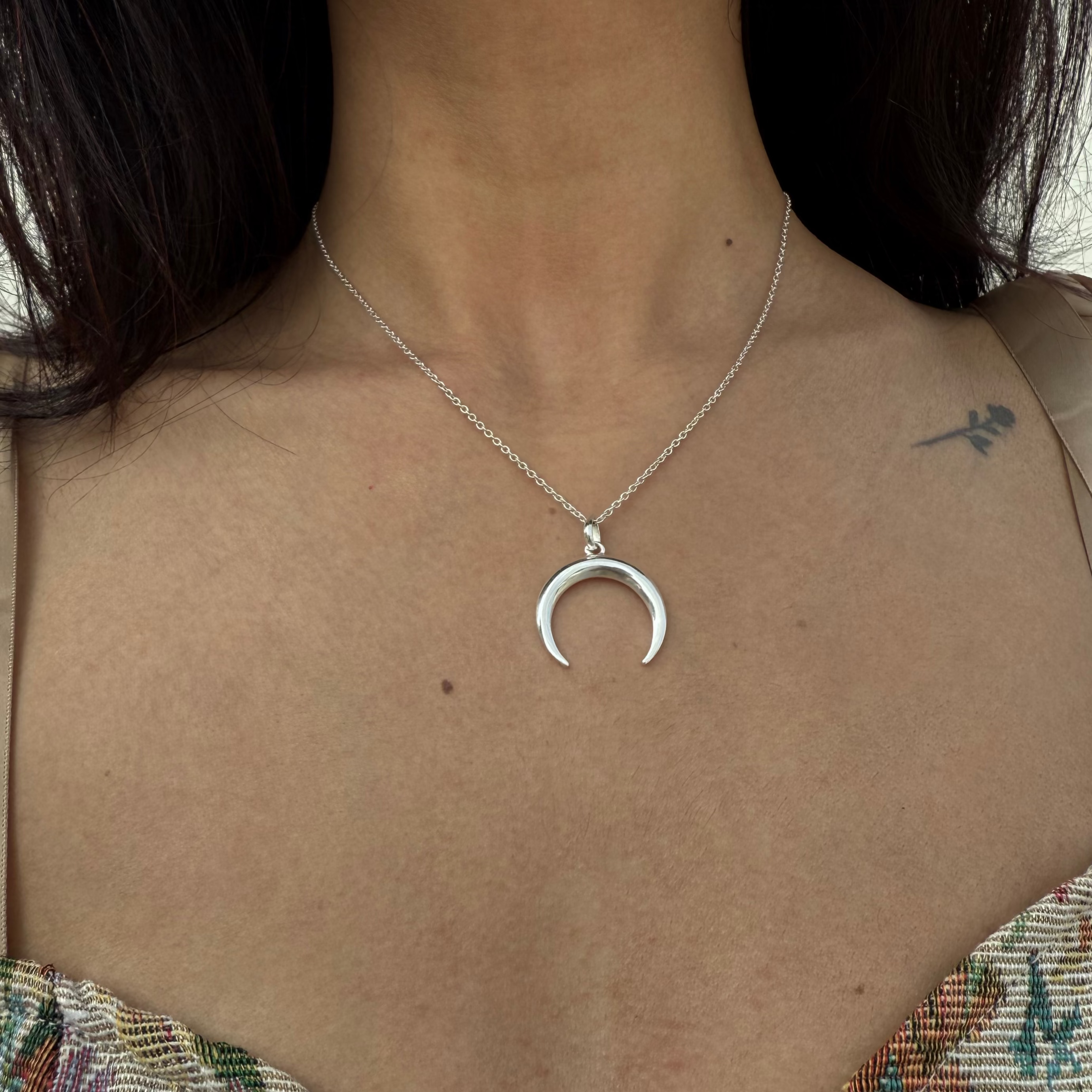 Silver crescent moon necklace worn by a person with a floral top.