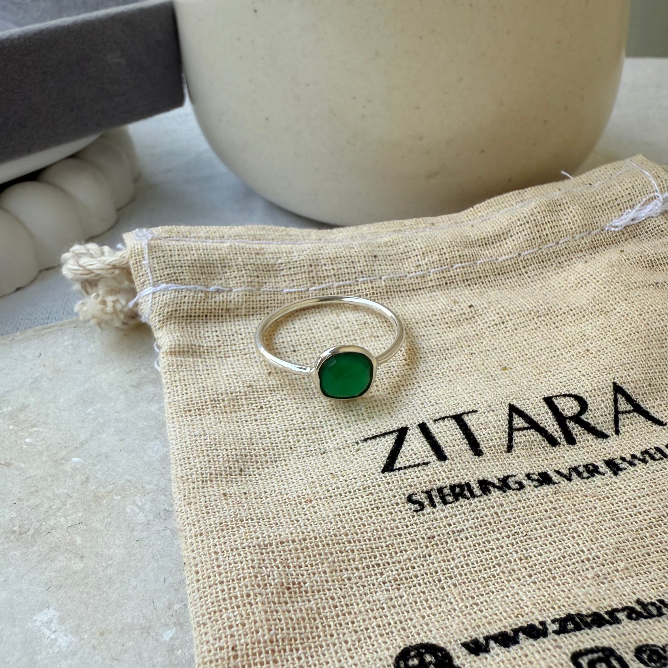 Silver ring with a green gemstone on a Zitara branded drawstring bag.