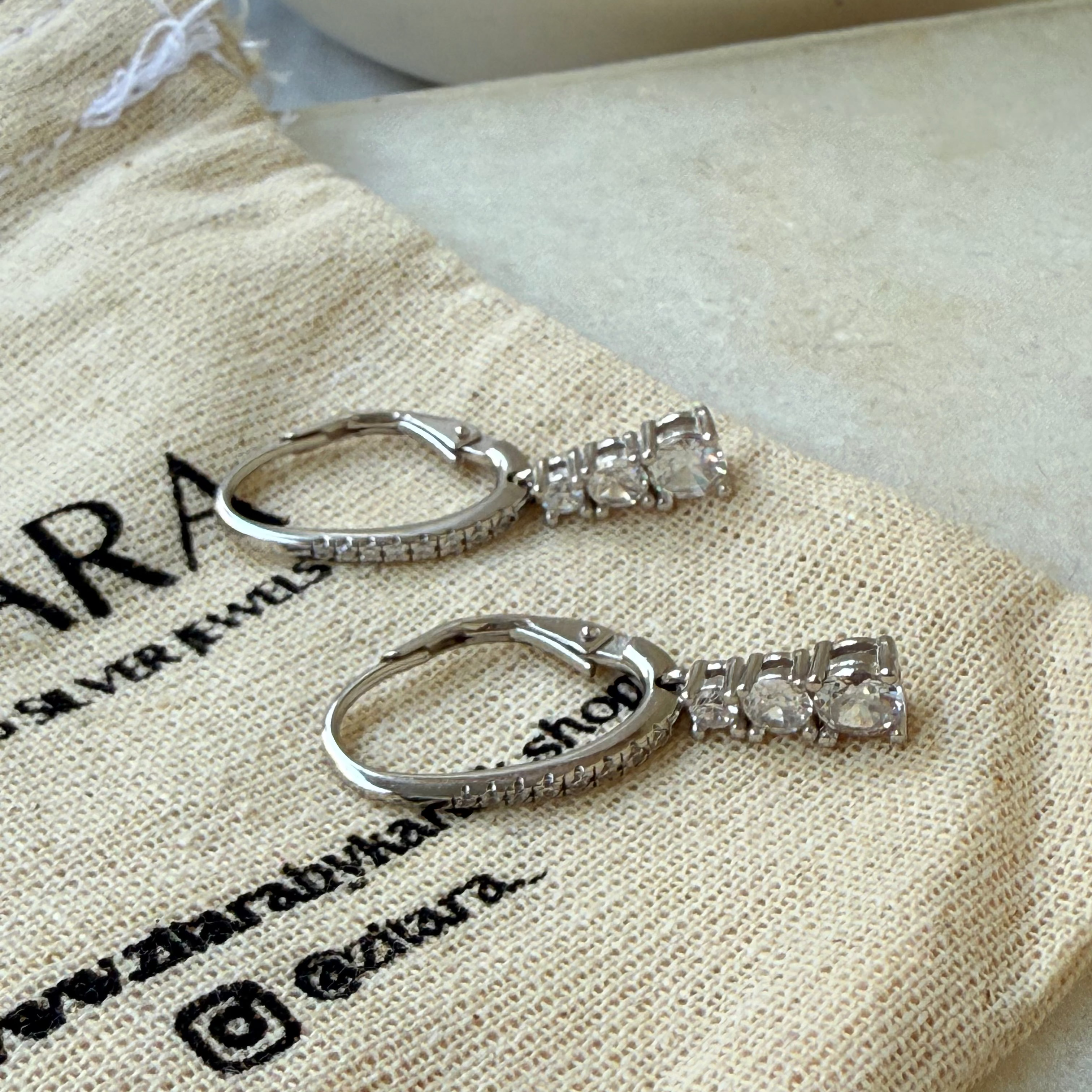 Silver earrings with clear stones on a Zara branded fabric background