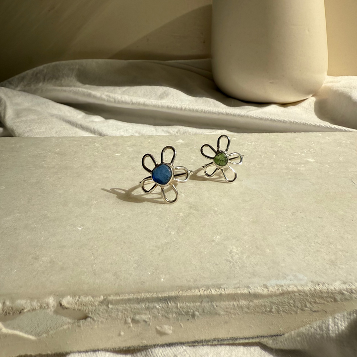 Flower-shaped earrings on a textured surface with a ceramic pitcher in the background.