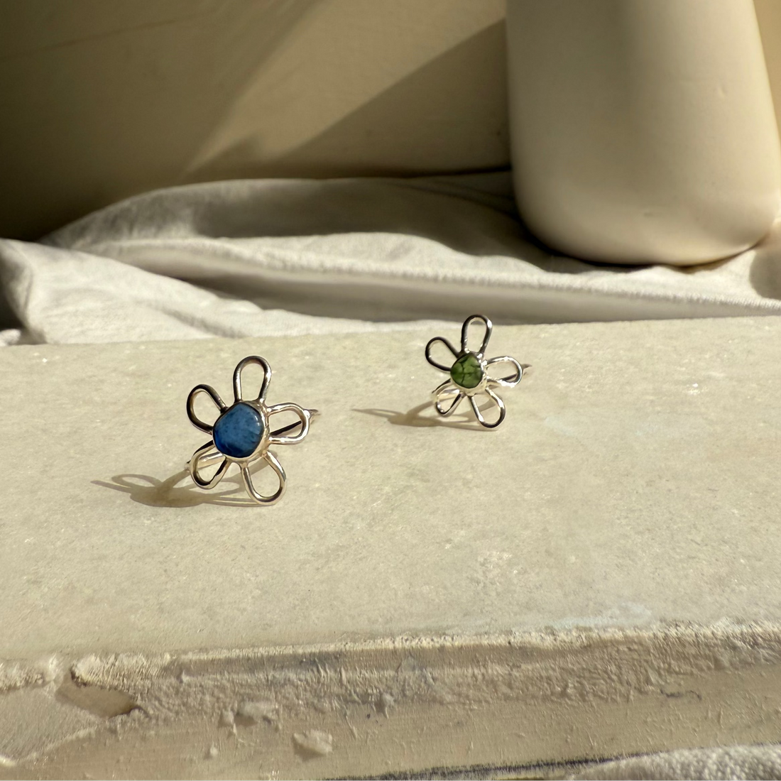 Two floral earrings on a textured surface with a vase in the background