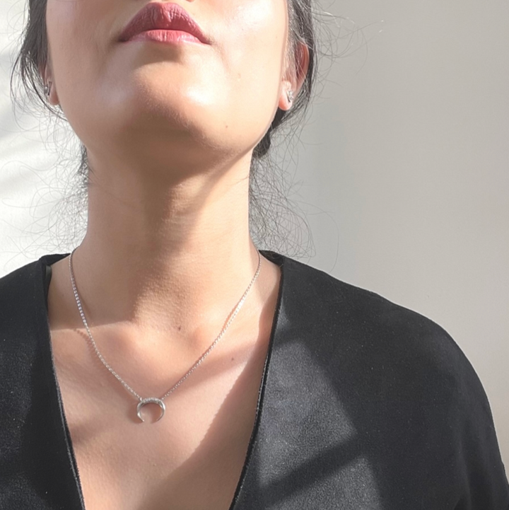 Person wearing a silver necklace with a small pendant against a neutral background