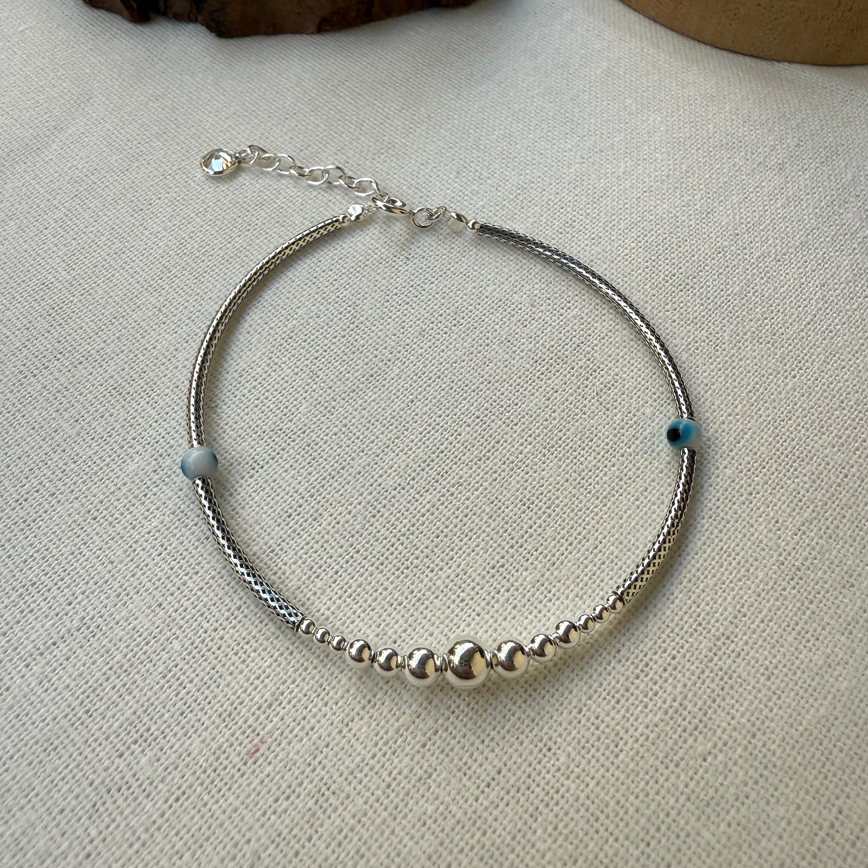 Silver beaded bracelet on a textured surface with wooden blocks in the background