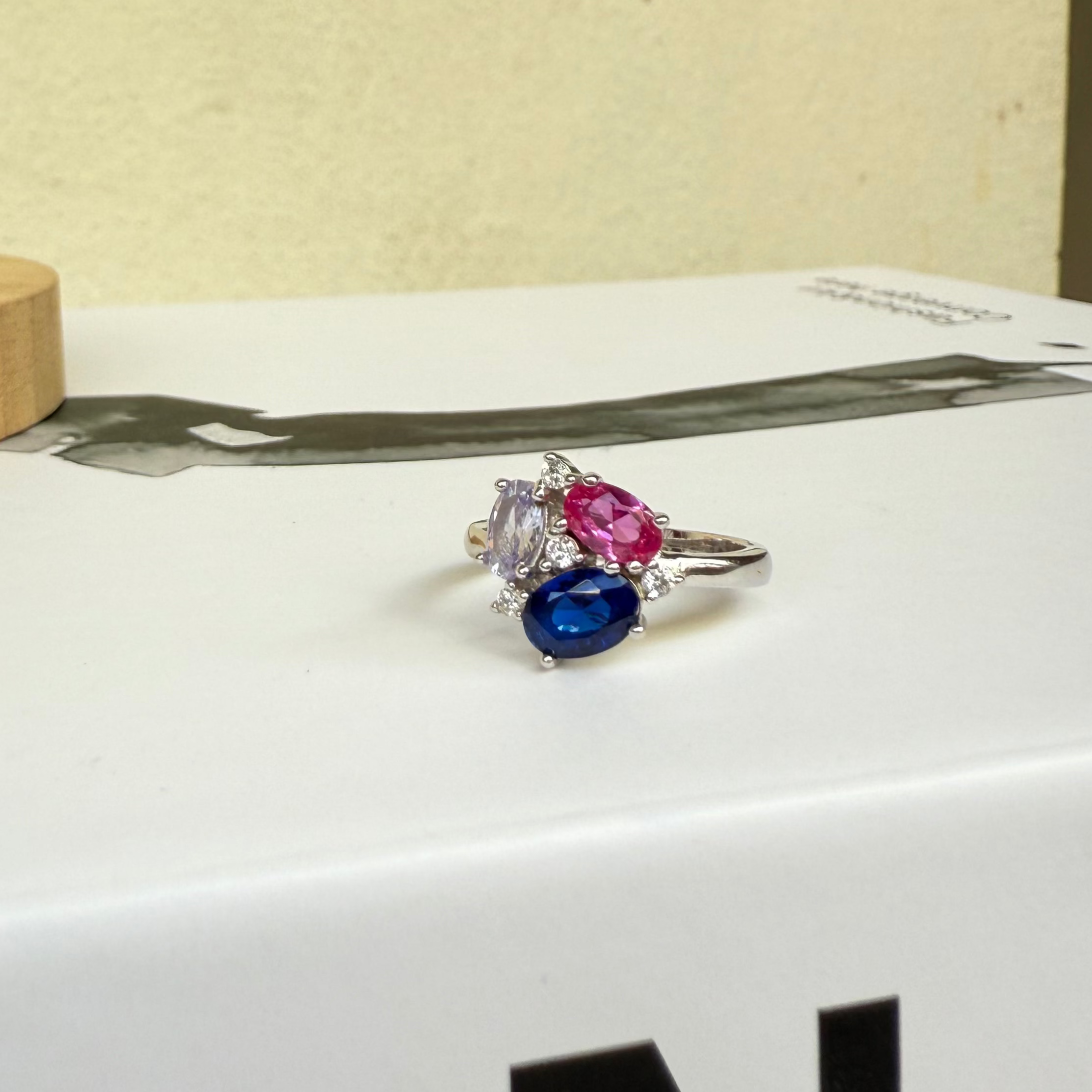 Ring with multicolored gemstones on a white surface with a wooden object in the background