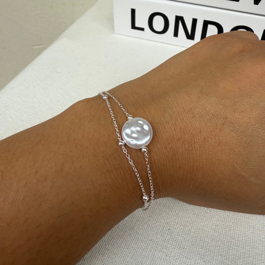 Silver bracelet on a wrist with 'LOEWE' branding in the background
