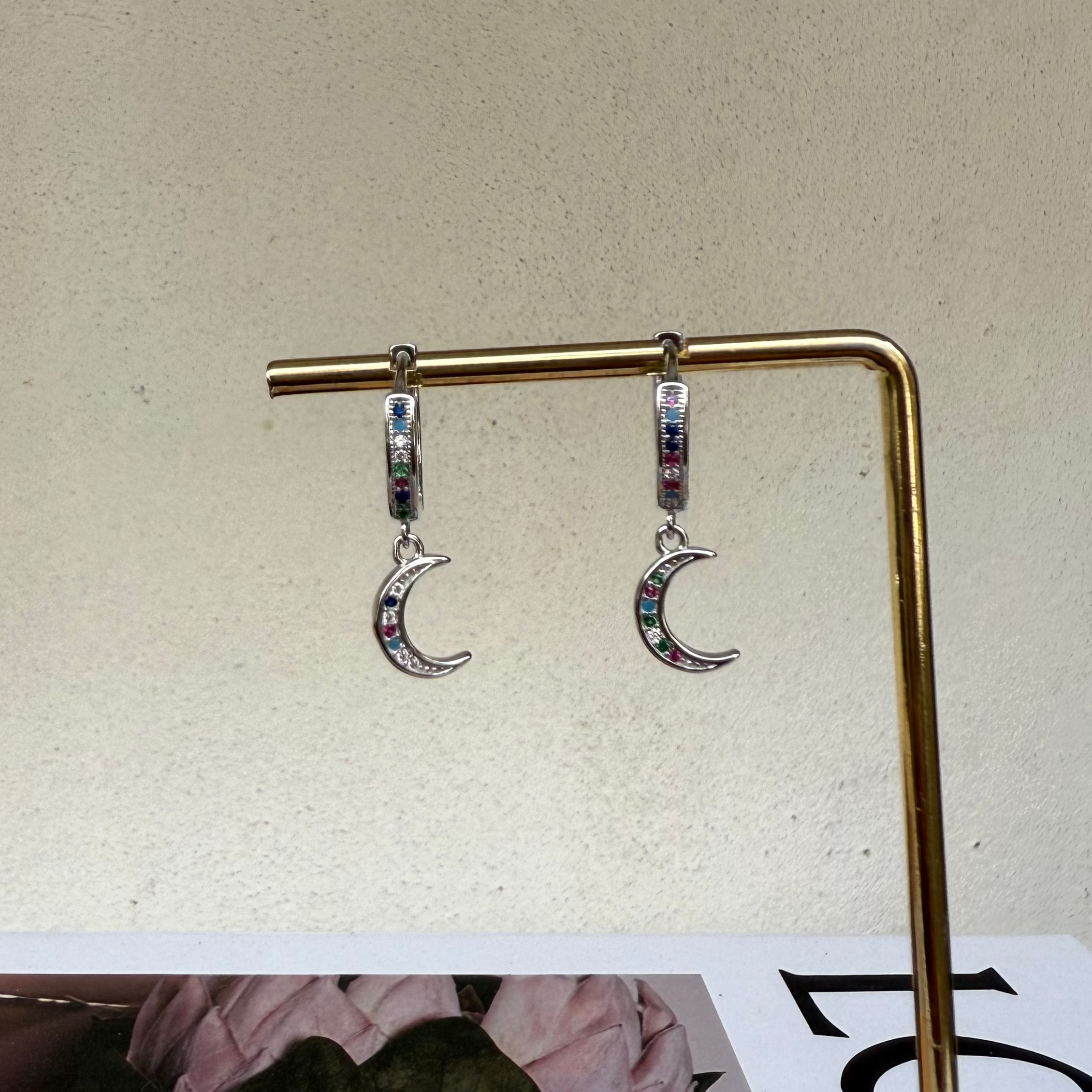 Moon-shaped earrings on a gold stand against a beige background