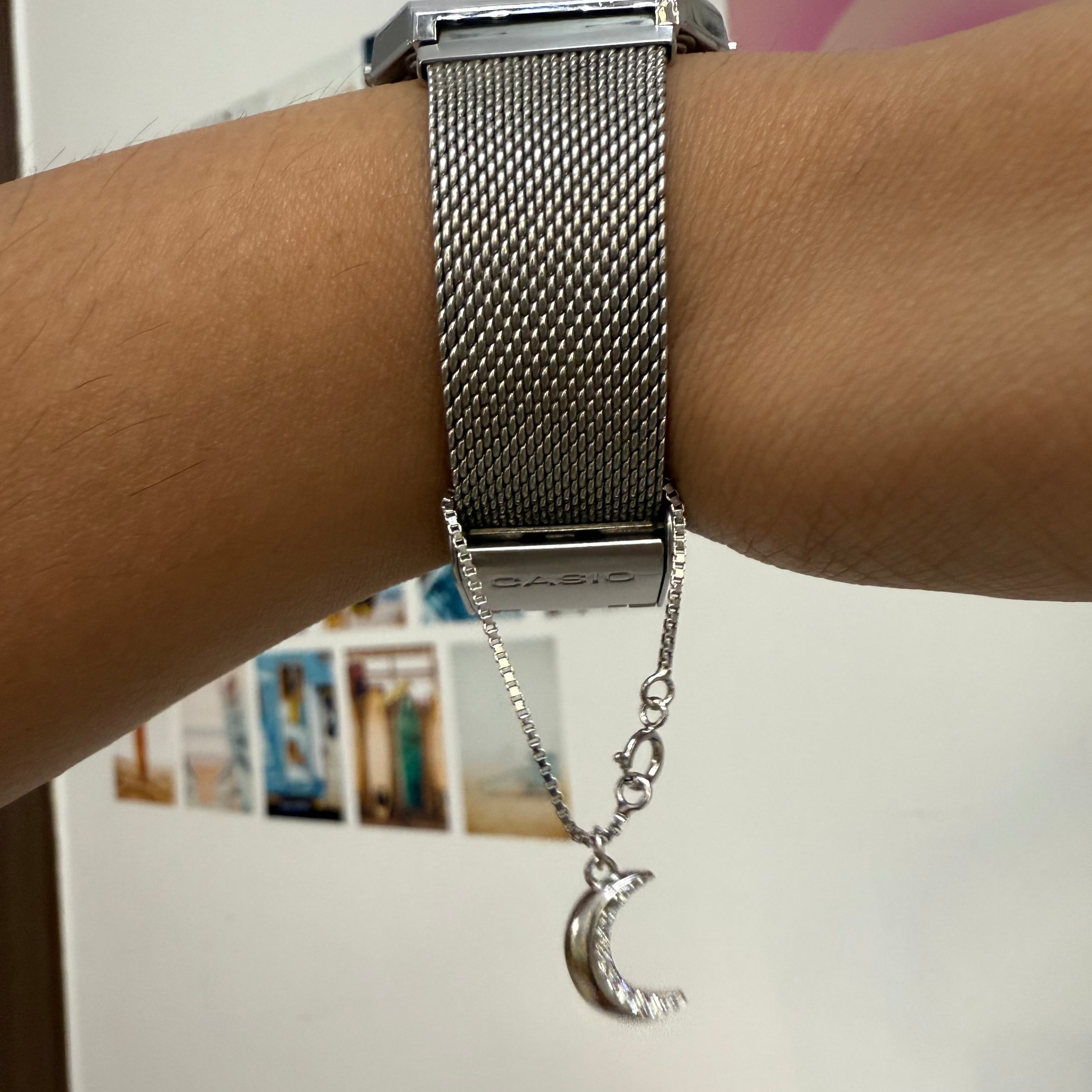 Silver watch with a moon and star charm on a wrist against a blurred background