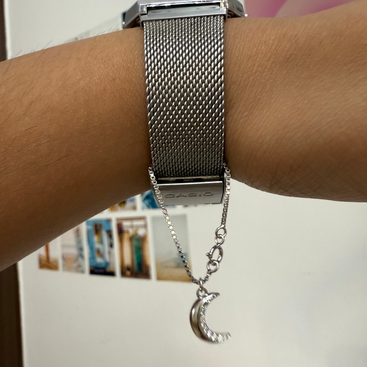 Silver watch with a moon and star charm on a wrist against a blurred background