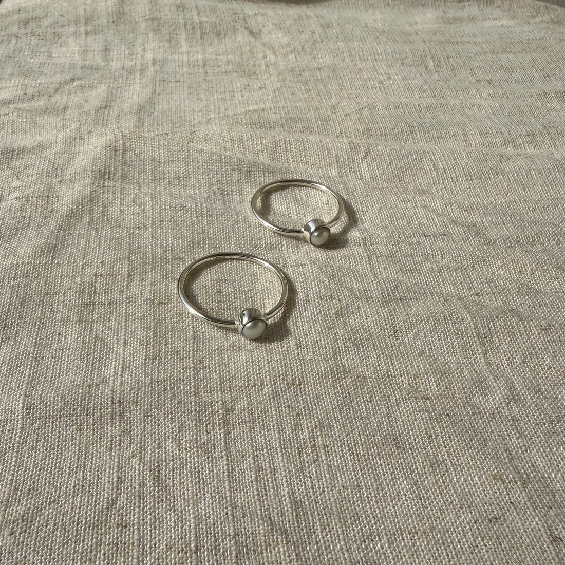 Two silver rings on a textured beige surface