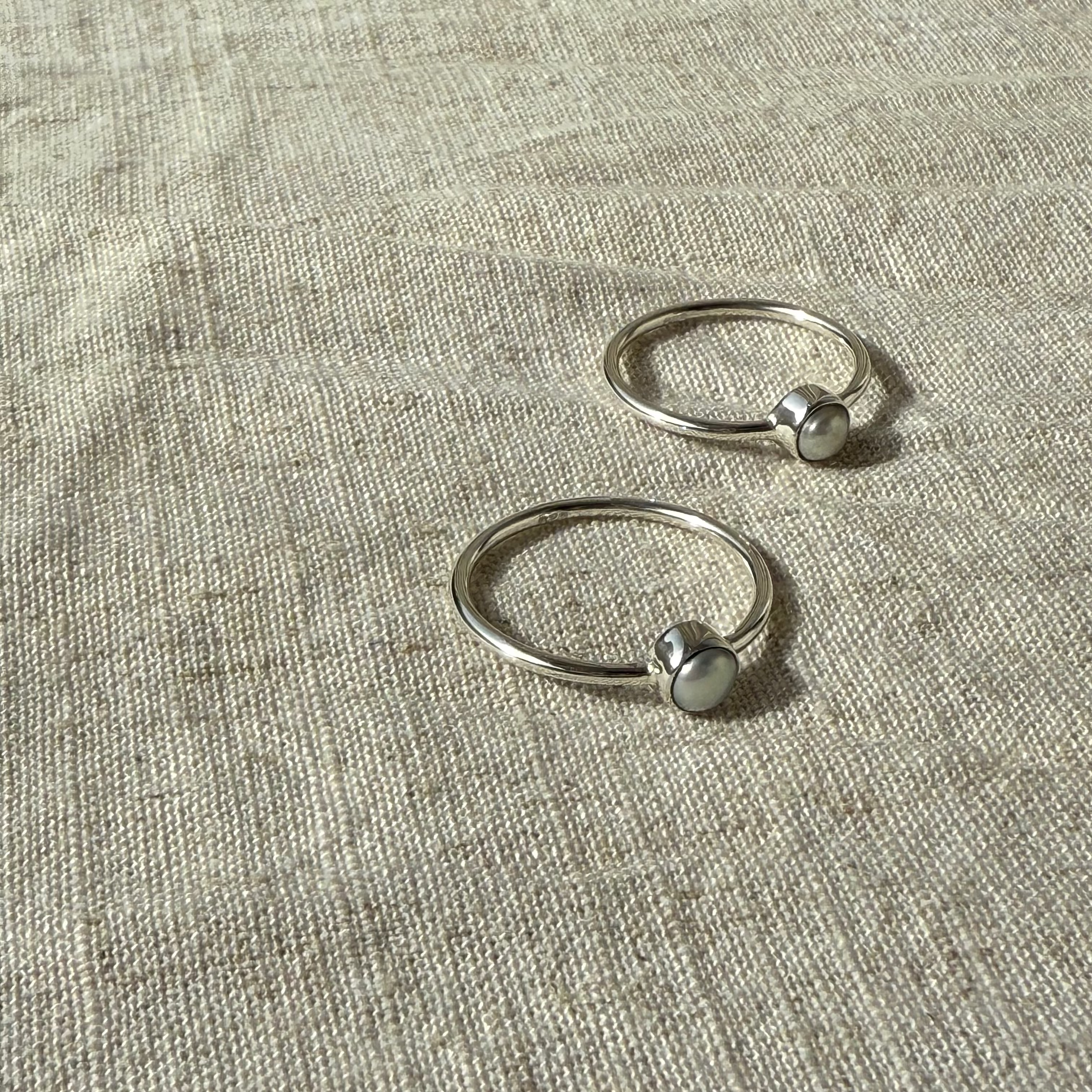Two silver rings with small spherical elements on a textured beige fabric background