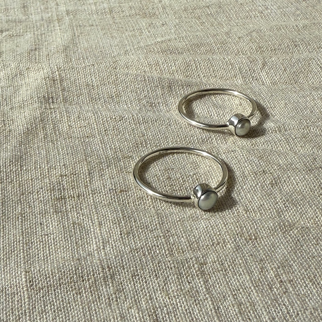 Two silver rings with small spherical elements on a textured beige fabric background