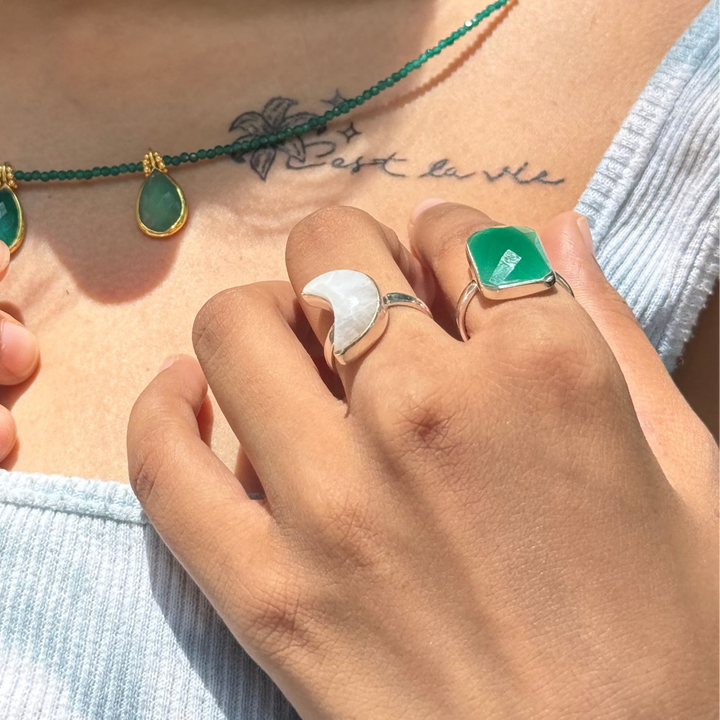 Close-up of hands wearing green and gold jewelry with a tattoo on the chest.
