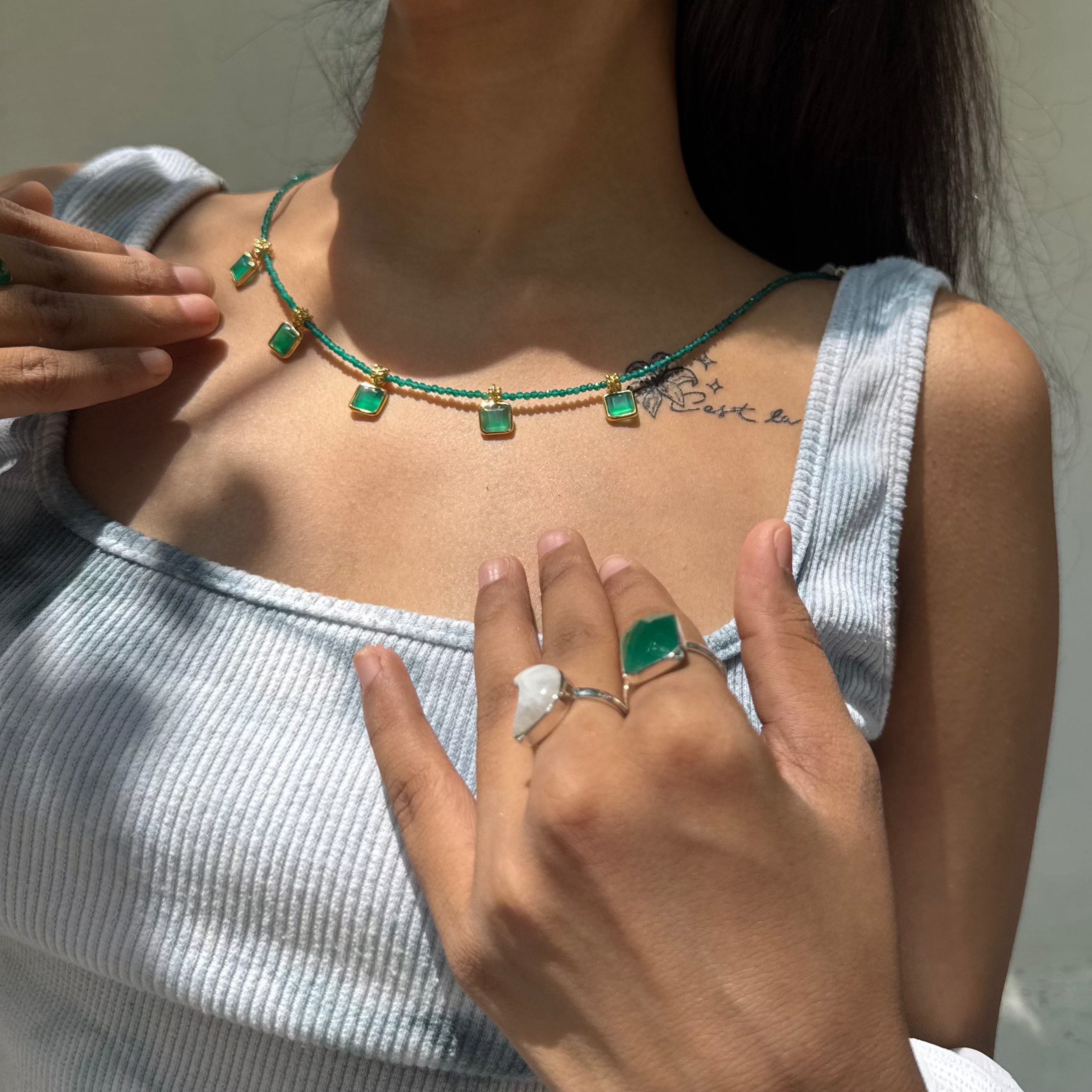 Woman wearing a green necklace and ring, with a blurred background