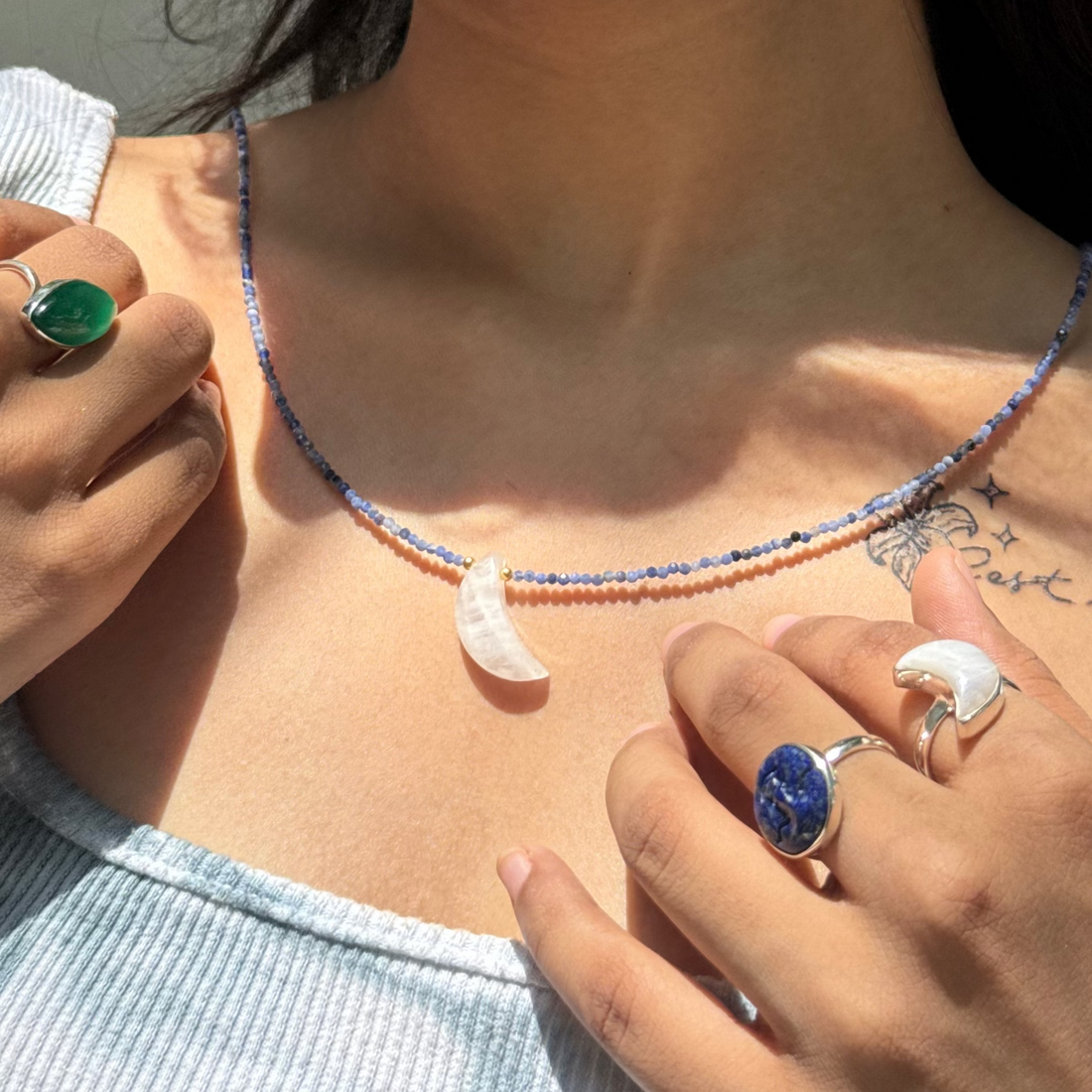 Woman wearing a necklace, rings, and earrings with a neutral background