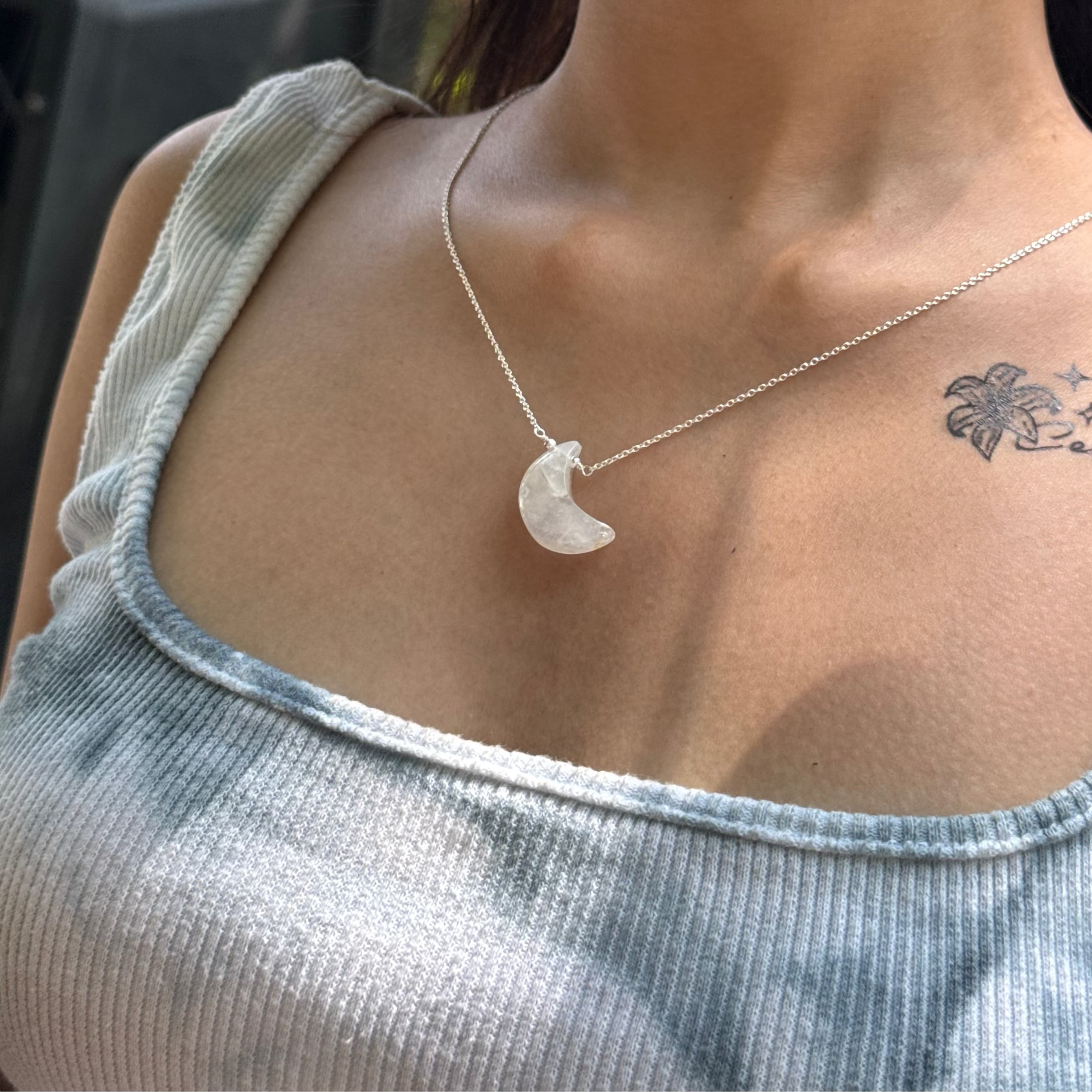Woman wearing a silver necklace with a crescent moon pendant, outdoors.