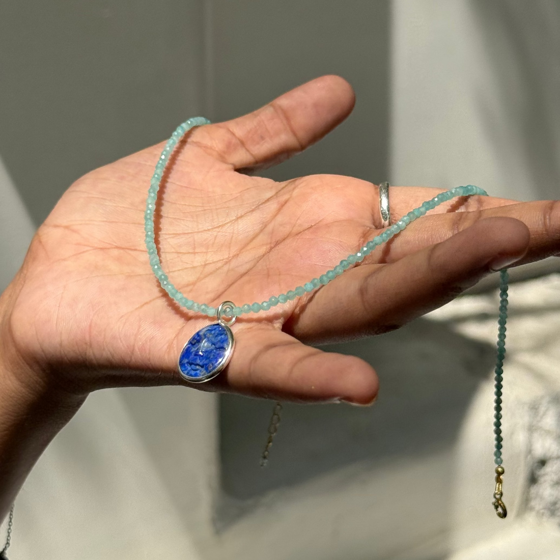Hand holding a blue beaded necklace against a neutral background