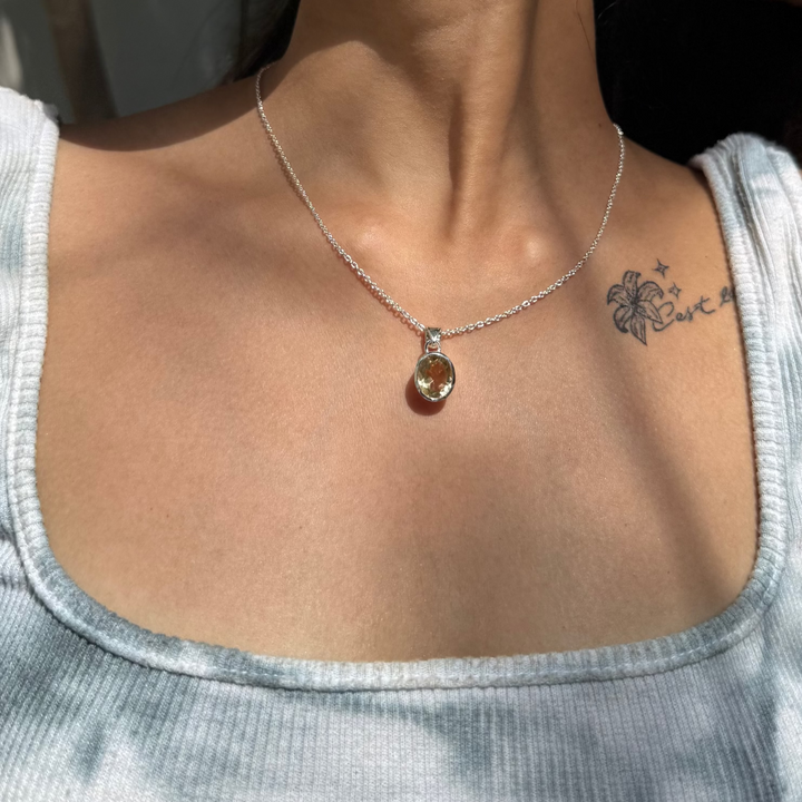 Necklace with a pendant worn by a person, with a tattoo visible on the neck.