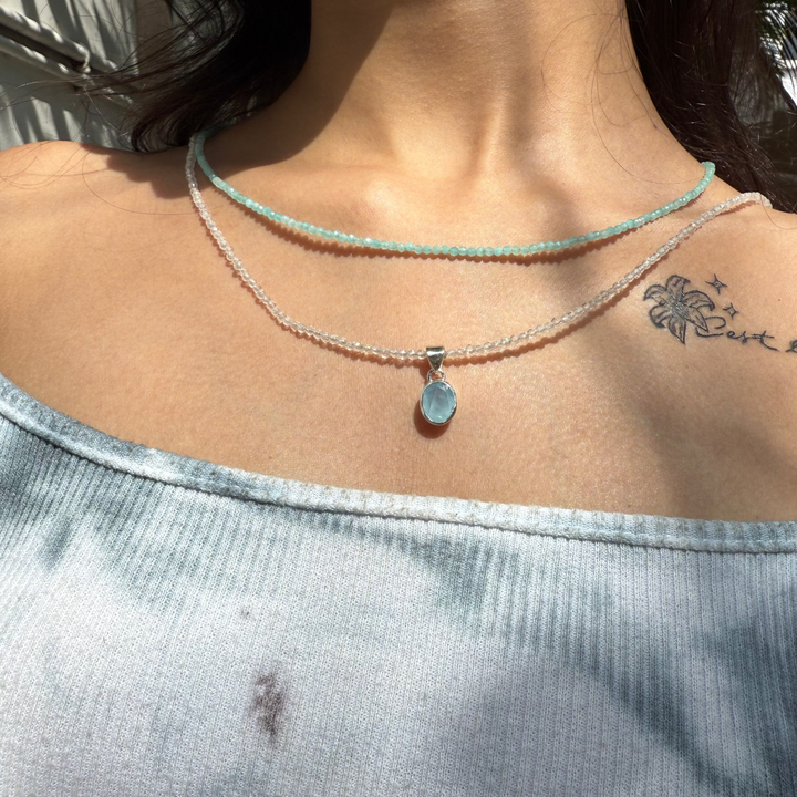 Close-up of a person wearing a delicate necklace with a small pendant, visible tattoo on shoulder