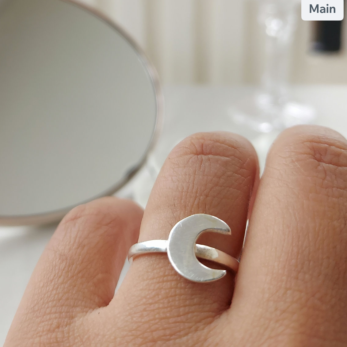 Silver ring with a moon design on a finger, blurred background